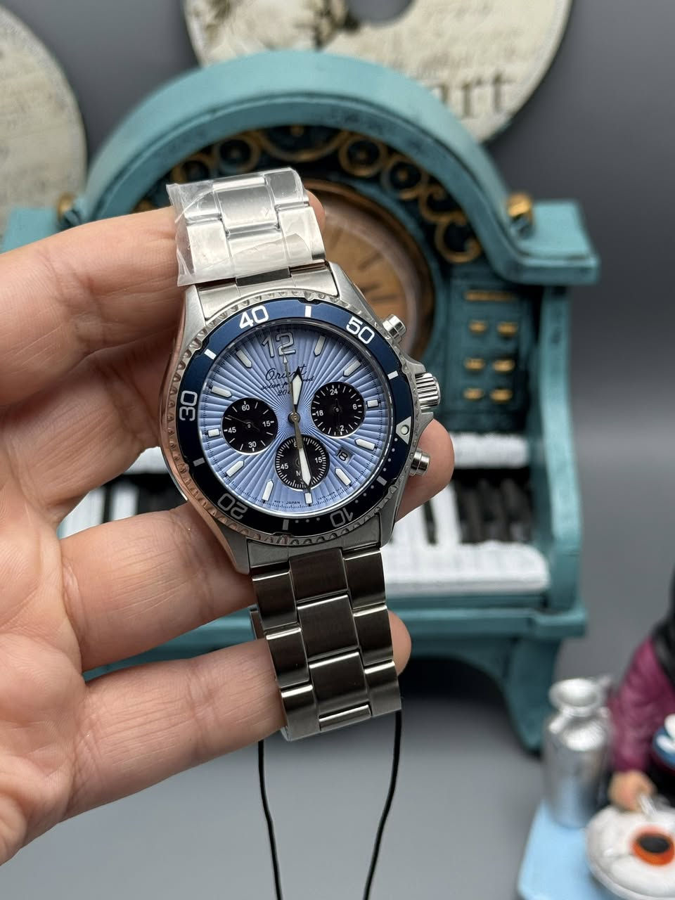 هذه الساعة التي تظهر في الصور هي إصدار خاص ومميز جداً من شركة أورينت (Orient) اليابانية العريقة، وتحديداً هي موديل Orient Mako Solar Chronograph بإصدار الذكرى الـ75 (75th Anniversary Limited Edition).
إليك شرح مفصل لمواصفاتها ومميزاتها:
1. التصميم العام والقرص (Dial)
• اللون والملمس: تتميز بقرص بلون "أزرق سماوي" فاتح مع نمط "Sunray" (أشعة الشمس) المحفور بشكل رائع، وهو تصميم مستوحى من الموديلات الكلاسيكية للشركة.
• الكرونوغراف: تحتوي على ثلاثة أقراص فرعية (Sub-dials) باللون الأسود، مما يعطي تبايناً جميلاً (يُعرف بستايل الباندا المعكوس).
• الإطار (Bezel): إطار دوار أحادي الاتجاه باللون الأزرق الداكن، يستخدم لحساب وقت الغوص أو الوقت المنقضي.
2. المواصفات التقنية (حسب ما يظهر على غطاء الساعة)
• نظام الحركة (Solar Powered): الساعة تعمل بالطاقة الشمسية. لا تحتاج لتغيير بطارية، حيث تشحن نفسها من أي مصدر ضوء (طبيعي أو صناعي).
• زجاج الياقوت (Sapphire Crystal): الزجاج مصنوع من السافير المقاوم للخدش، وهو من أفضل أنواع الزجاج المستخدمة في الساعات لضمان بقائها كالجديدة لفترة طويلة.
• مقاومة الماء (Water Resistant 20bar): الساعة مقاومة للماء حتى عمق 200 متر، مما يجعلها مناسبة جداً للسباحة والغوص السطحي.
• المعدن: الهيكل والسوار مصنوعان من الفولاذ المقاوم للصدأ (Stainless Steel) عالي الجودة.
3. مميزات الإصدار المحدود (Limited Edition)
• الذكرى الـ75: تم إصدار هذه الساعة خصيصاً للاحتفال بمرور 75 عاماً على تأسيس شركة أورينت (1950-2025).
• العدد المحدود: يظهر على الغطاء الخلفي رقم التسلسل الخاص بها (0667 / 1000)، مما يعني أنه تم إنتاج 1000 قطعة فقط من هذا الموديل في العالم، وهذه الساعة هي رقم 667.
• نقش خاص: الغطاء الخلفي يحمل شعار الذكرى الـ75 واسم شركة "EPSON" (الشركة الأم الحالية لأورينت).
لماذا تعتبر هذه الساعة قيمة؟
1. جامعي الساعات: لكونها إصداراً محدوداً بـ 1000 قطعة فقط، فقيمتها تزداد مع مرور الوقت كقطعة نادرة.
2. العملية: تجمع بين مظهر ساعات الغوص الرياضية ووظيفة الكرونوغراف، مع ميزة الشحن الشمسي التي تجعلها مريحة جداً للاستخدام اليومي.
3. الجودة: استخدام زجاج السافير ومقاومة الماء العالية يجعلها ساعة "كرف" تتحمل الظروف الصعبة.

للحجز والاستفسار 
***********

تك توك 

https://www.tiktok.com/@harmonytime.iq?_r=1&_t=ZS-930lLTOVA16
