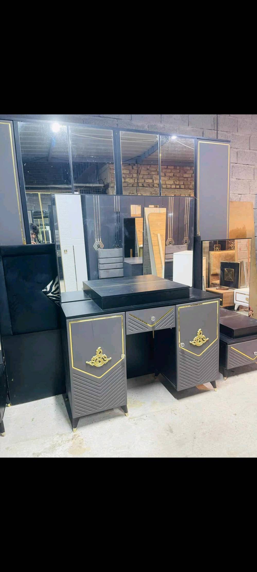 شروط جديدة مودرن، غرفة نوم متكاملة تظم سرير بتنجيد مميز، دولاب ملابس أنيق بمرايا تغطي الأبواب، وتواليت متعدد الأدراج. تفاصيل الحفر الذهبي تضيف لمسة من الفخامة، مما يجعلها خياراً مثالياً للمنازل الحديثة والمتجددة.