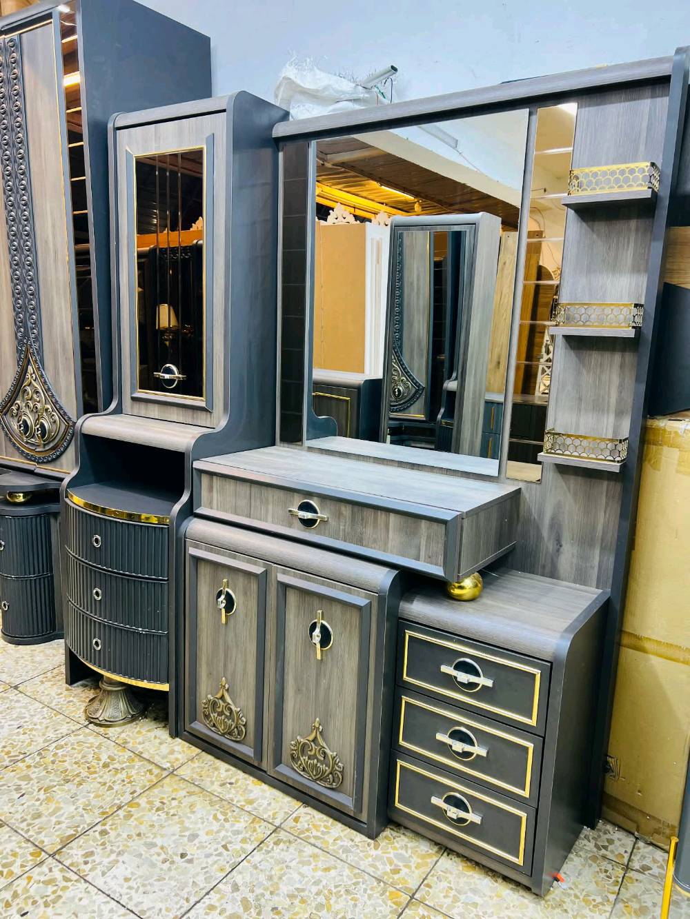 غرفة نوم مودرن وجديدة للبيع، تتميز بتصميم راقي وأنيق بلون رمادي مع لمسات ذهبية. تحتوي الغرفة على خزانة ملابس واسعة مع مرايا، وتسريحة مع أدراج ووحدات تخزين متعددة بالإضافة إلى طاولات جانبية بتصميم جمالي لتكمل الديكور. تناسب مختلف الأذواق وتضيف لمسة من الفخامة لأي منزل.