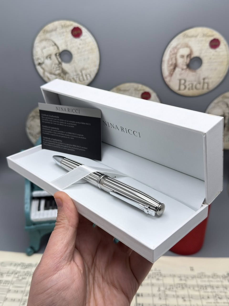 نينا ريتشي (Nina Ricci). هذه الأقلام تُعرف بكونها إكسسوارات فاخرة تجمع بين الأناقة الباريسية والعملية.
إليك شرح مفصل لما تظهره الصور:
1. العلامة التجارية والجودة
• الماركة: Nina Ricci هي دار أزياء راقية، وأقلامها تُصنف كأدوات كتابة "برستيج" (Prestige).
• الأصالة: يظهر في الصور "شهادة أصالة" (Certificate of Authenticity)، مما يؤكد أن القلم أصلي ويأتي مع ضمان (غالباً لمدة سنتين ضد عيوب التصنيع).
2. التصاميم والموديلات الظاهرة
من خلال الصور، نرى أربعة أشكال مختلفة، مما يوفر خيارات متنوعة للأذواق:
• القلم الأول (بني مموج): يتميز بنقشة "Tortoise" أو التورتويز (صدفة السلحفاة) الكلاسيكية مع لمسات معدنية داكنة. هذا التصميم يوحي بالفخامة التقليدية والمظهر الدافئ.
• القلم الثاني (أسود وفضي): تصميم كلاسيكي "مينيماليست" باللون الأسود اللامع مع حواف فضية، وهو مثالي لرجال الأعمال والمناسبات الرسمية.
• القلم الثالث (ذهبي مخطط): قلم باللون الذهبي الكامل مع خطوط طولية محفورة، يعطي طابعاً ملكياً لافتاً للنظر.
• القلم الرابع (فضي/كروم مخطط): مشابه للذهبي ولكن باللون الفضي، يتميز بالهدوء والعصرية، ومقاوم بشكل جيد للخدوش بفضل المادة المعدنية.
3. المواصفات الفنية
• نوع القلم: يظهر من الرؤوس أنها أقلام حبر جاف (Ballpoint) تعمل غالباً بآلية التدوير (Twist mechanism) لفتح وإغلاق القلم.
• الخامات: الهيكل عادة ما يكون مصنوعاً من النحاس المطلي بالروديوم، الذهب، أو الورنيش عالي الجودة (Lacquer).
• التغليف: يأتي في علبة بيضاء فاخرة مبطنة من الداخل بكلمة "NINA RICCI" مطبوعة بشكل أنيق، مما يجعله خياراً ممتازاً للهدايا.
4. مميزات الاقتناء
• الوزن: هذه الأقلام تمتاز بوزن متزن (ليست خفيفة جداً ولا ثقيلة)، مما يوفر راحة أثناء الكتابة الطويلة.
• سهولة التعبئة: تستخدم عبوات حبر قياسية متوفرة بسهولة في المكتبات الكبرى.
• القيمة: يعتبر قطعة إكسسوار تكمل المظهر الشخصي، تماماً مثل الساعة أو المحفظة.

للحجز والاستفسار 
***********
