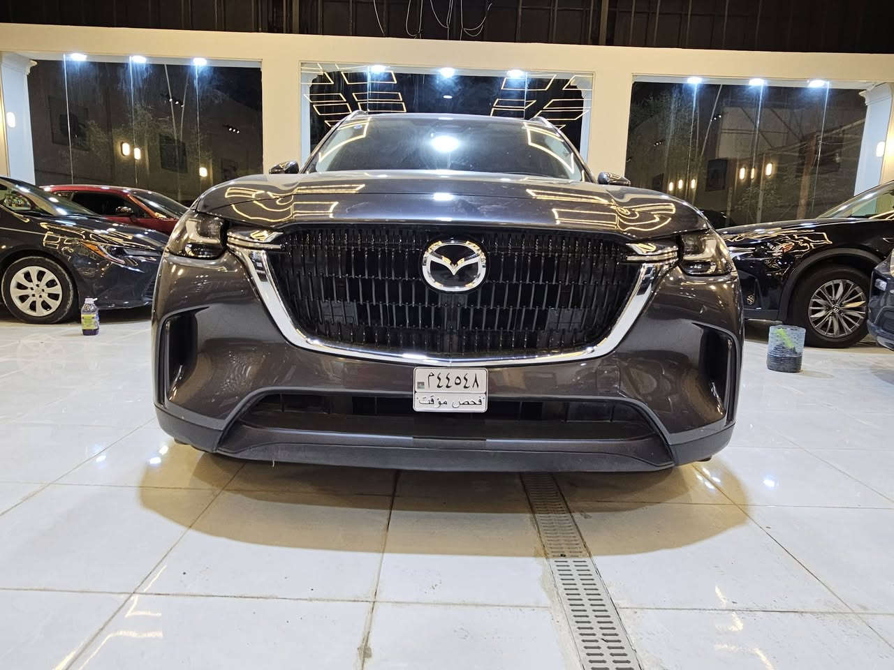 سيارة **مازدا CX-90 موديل 2024** بمحرك الـ 6 سلندر هجين (Mild Hybrid)  حيث تعتمد على محرك طولي ونظام دفع رباعي موجه للخلف لتحقيق أداء رياضي وفخم..
إليك أهم المواصفات التقنية والمميزات:
### 1. المحرك والأداء (e-Skyactiv G)
تتوفر بمحرك 6 أسطوانات متتالية (Inline-6) سعة 3.3 لتر مع شاحن تيربو، مدعوم بنظام هجين بسيط (48 فولت):
 * **القوة الحصانية:** تتوفر بخيارين حسب الفئة:
   * **الفئة القياسية:** 280 حصان وعزم دوران 450 نيوتن متر.
   * **الفئة العالية (S):** تصل إلى 340 حصان وعزم دوران 500 نيوتن متر (وهي أقوى سيارة إنتاجية من مازدا).
 * **ناقل الحركة:** أوتوماتيكي من 8 سرعات (جديد كلياً بدون محول عزم تقليدي لتوفير استجابة أسرع).
 * **نظام الدفع:** دفع كلي للعجلات (i-Activ AWD) بشكل قياسي.
 * **التسارع:** من 0 إلى 100 كم/ساعة في حوالي **5.8 إلى 6.5 ثانية** (حسب القوة).
### 2. استهلاك الوقود
 * تعتبر اقتصادية مقارنة بحجمها بفضل النظام الهجين، حيث تستهلك وسطياً حوالي **9.3 إلى 9.4 لتر لكل 100 كم**.
 * سعة خزان الوقود: **74 لتر**.
### 3. الأبعاد والمساحة
 * **الطول:** حوالي 5.1 متر، مما يجعلها سيارة SUV كبيرة بـ 3 صفوف من المقاعد.
 * **السعة:** تتوفر بخيارات 6 أو 7 أو 8 ركاب حسب التوزيع الداخلي.
 * **مساحة الأمتعة:** 608 لتر (خلف الصف الثالث) وتصل إلى 2025 لتر عند طي المقاعد.
### 4. التكنولوجيا والمقصورة الداخلية
 * **الشاشات:** شاشة مركزية كبيرة مقاس 12.3 بوصة تدعم Apple CarPlay و Android Auto لاسلكياً.
 * **النظام الصوتي:** يتوفر نظام Bose بـ 12 مكبر صوت في الفئات العليا.
 * **المواد:** استخدام جلود النابا، الأخشاب الطبيعية، وتطريزات مستوحاة من الفن الياباني التقليدي.
 * **ميزات إضافية:** فتحة سقف بانورامية، شاشة عرض على الزجاج الأمامي (Head-up Display)، وشحن لاسلكي.
### 5. أنظمة الأمان (i-Activsense)
 * نظام تثبيت السرعة التكيفي (الرادار).
 * نظام المساعدة في البقاء في المسار وتنبيه الخروج منه.
 * مكابح الطوارئ التلقائية مع رصد المشاة.
 * كاميرات 360 درجة مع خاصية "See-Through" لرؤية ما تحت السيارة أو حولها بوضوح.

**ملاحظة للمهتمين بالصيانة:** بما أنك تتابع تفاصيل المحركات بدقة، فإن هذا المحرك (Inline-6) مصمم ليكون متوازناً طبيعياً وأقل اهتزازاً من محركات الـ V6، وهو ما يعطي سلاسة تشبه محركات السيارات الألمانية الفاخرة.
ضررها  كفاله عامه تقرير مياه امطار تعمل وتسير
عداد المسافات ٤٠٠٠
للاستفسار معرض بلاتينيوم لتجارة السيارات  سامراء 
للاستفسار ***********
سيارة **مازدا CX-90 موديل 2024** بمحرك الـ 6 سلندر هجين (Mild Hybrid)  حيث تعتمد على محرك طولي ونظام دفع رباعي موجه للخلف لتحقيق أداء رياضي وفخم..

