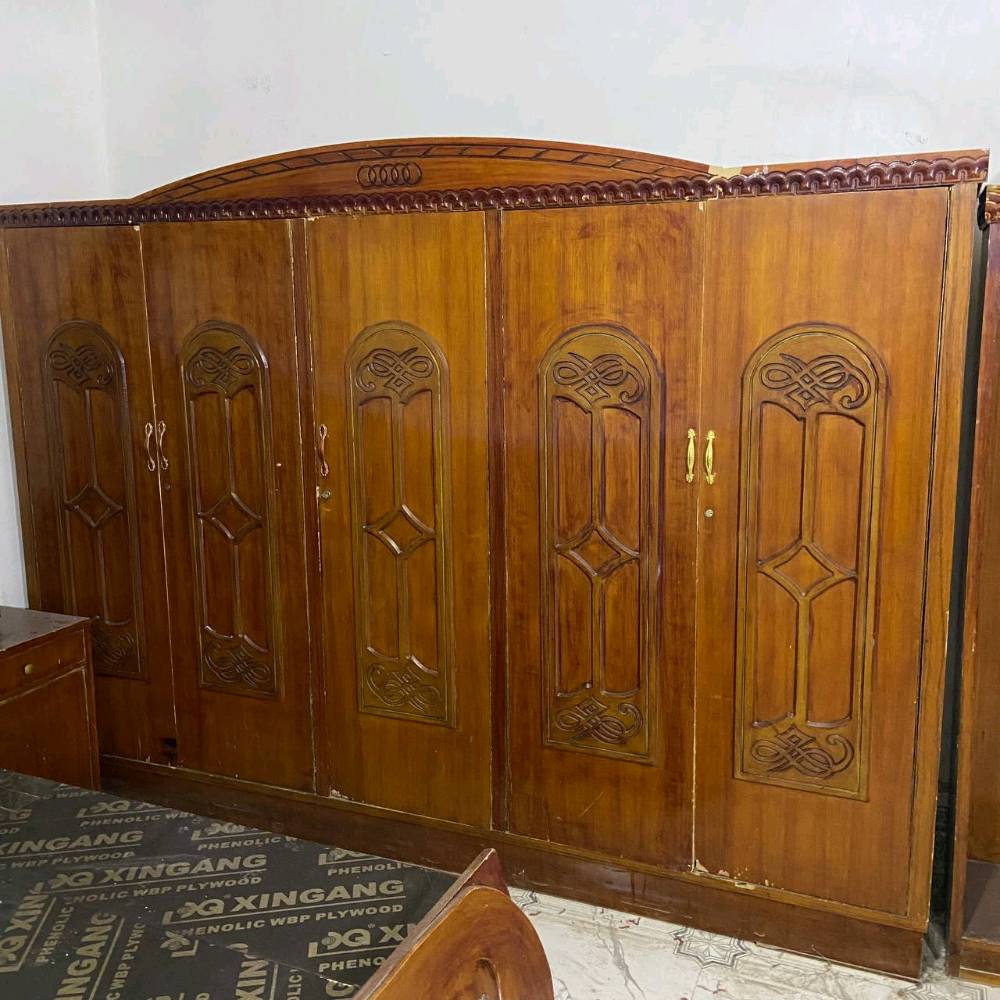 غرفة نوم خشبية كلاسيكية مكونة من سرير مع مرآة فاخرة ودولاب مكون من عدة أبواب. التصميم يحتوي على حفرات ونقوش جميلة تضيف لمسة مميزة للغرفة. الأثاث بحالة جيدة ومناسب لإضافة جمالية لأي غرفة نوم.