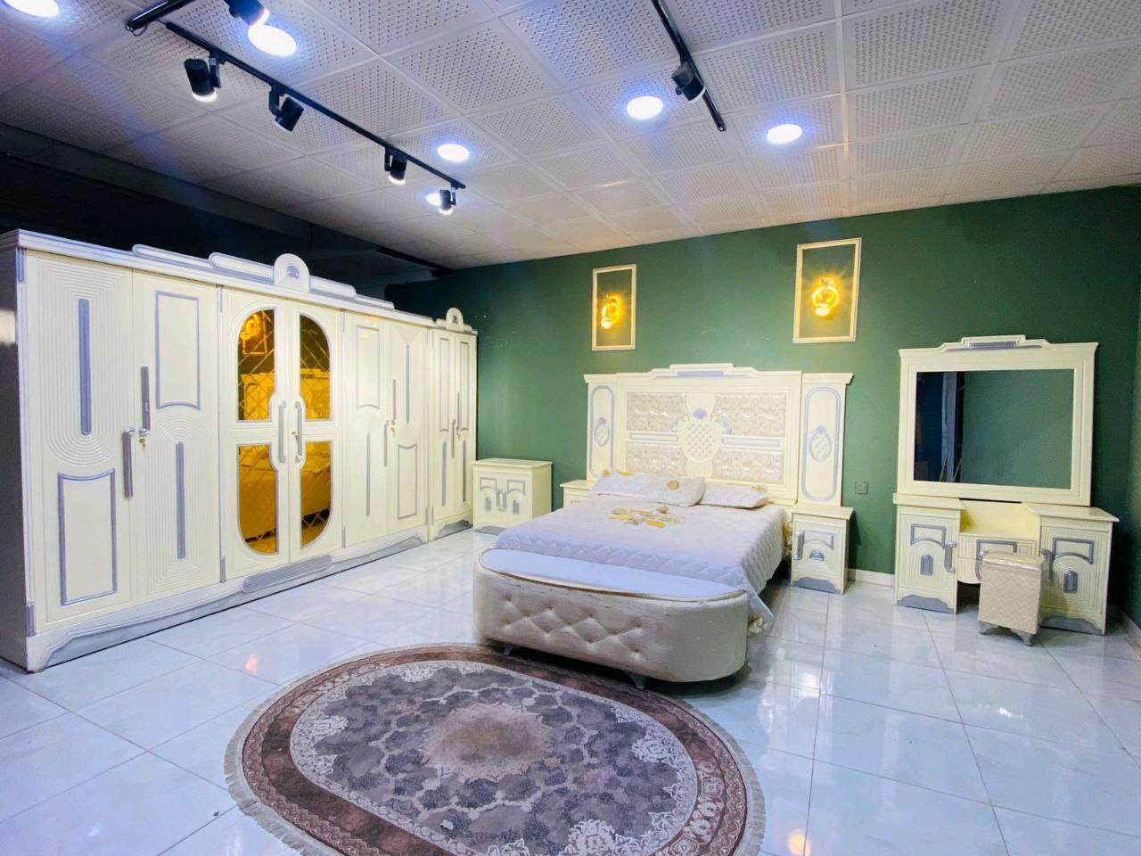 غرفة نوم فاخرة بتصميم كلاسيكي جذاب تتميز بمظهر أنيق وفخم. تضم سرير واسع ودولاب ملابس كبير مع مرايا، بالإضافة إلى طاولة زينة ودواليب جانبية بنفس التصميم. الخامات المستخدمة تعطي مظهر دافئ ومريح، مثالي لإضفاء لمسة من الفخامة في غرفة نومك.