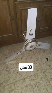 مروحة سقف بثلاث شفرات بلون أبيض مع تفاصيل ذهبية جميلة. مثالية لتهوية ا...