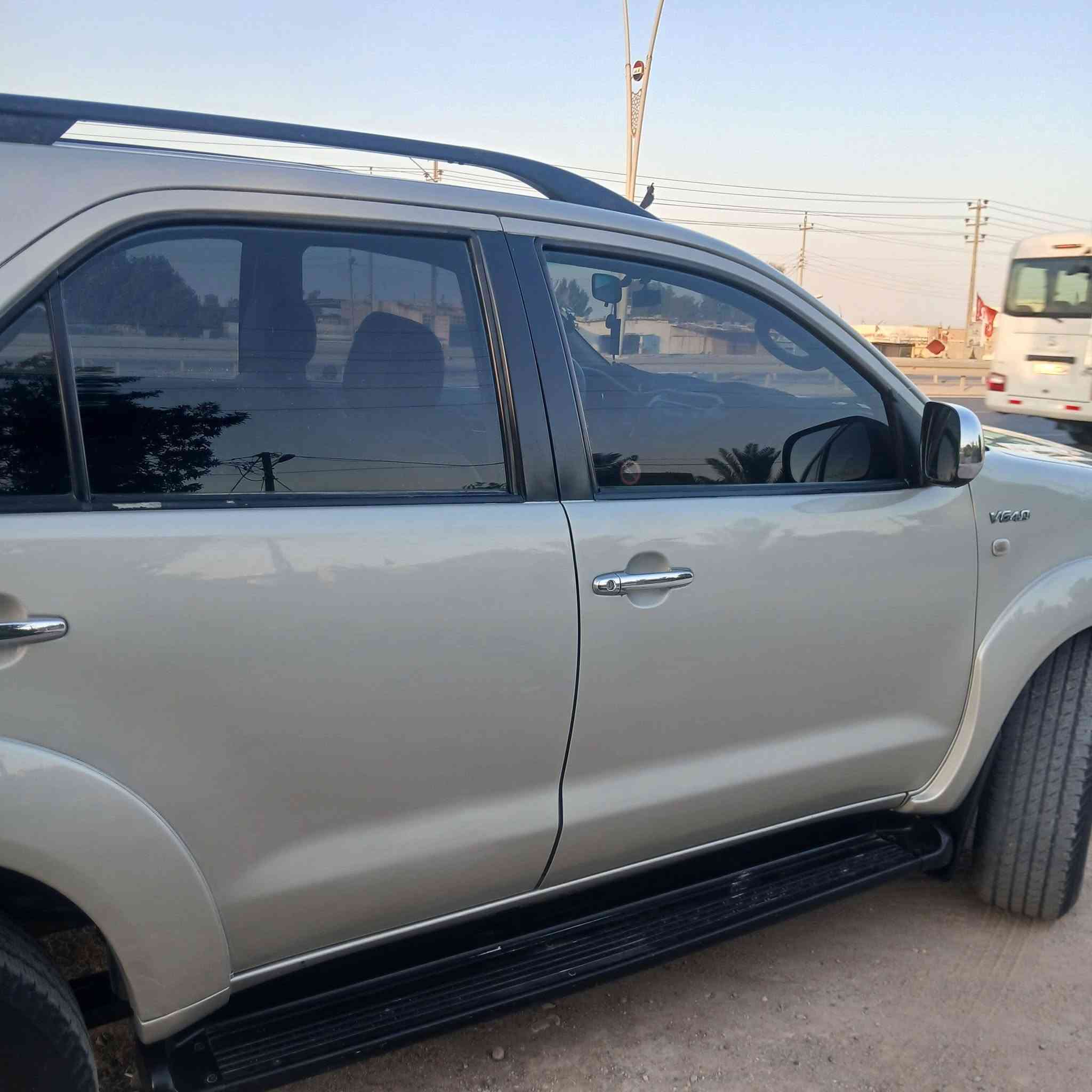 السيارة الظاهرة في الصورة "1000372575.jpg" هي تويوتا فورتشنر (Toyota Fortuner) من الجيل الأول (تحديداً الموديلات بين 2005 و 2008 قبل التحديث الأول). وهي سيارة SUV مخصصة للمهام الشاقة تعتمد على شاسيه "تويوتا هايلوكس".
إليك المواصفات الكاملة والعامة لهذا الجيل:

​1. المحرك والأداء (تأتي بخيارين رئيسيين للمحركات)

​المحرك الأول (٦ سلندر): سعة 2.7 لتر (2TR-FE) بقوة حوالي 158 حصان.

​المحرك الثاني (6 سلندر - V6): سعة 4.0 لتر (1GR-FE) بقوة حوالي 235 حصان (وهو الأكثر انتشاراً للفئات العالية).

​ناقل الحركة: آلي (أوتوماتيك) من 4 أو 5 سرعات، أو يدوي من 5 سرعات.

​نظام الدفع: دفع رباعي مستمر (4WD) مع ناقل حركة يدوي إضافي لتغيير وضعيات الدفع (الدبل الثقيل والخفيف)، وتتوفر ببعض الأسواق بدفع ثنائي خلفي فقط.

​2. الأبعاد والتصميم الخارجي

​النوع: سيارة رياضية متعددة الاستخدامات (SUV) متوسطة الحجم بـ 5 أبواب.

​المظهر الأمامي (كما في الصورة): شبك أمامي بلمسات كروم، ومصابيح أمامية هالوجين كبيرة، وكشافات ضباب سفلية مدمجة في المصد.

​الإضافات الظاهرة في الصورة: تم تركيب مصد حماية أمامي معدني (دعامية) لحماية الواجهة، وقضبان سقفية (Roof Rails).

​3. المقصورة والراحة الداخلية

​السعة: تتسع لـ 7 ركاب (ثلاثة صفوف من المقاعد).

​التكييف: نظام تكييف قوي جداً (هوائي مزدوج أمامي وخلفي لتغطية الصفوف الثلاثة).

​المقاعد: مخمل (قماش) في الفئات القياسية، وجلد في الفئات الكاملة (المواصفات العالية).

​4. الأمان والسلامة

​وسائد هوائية أمامية (Airbags) للسائق والراكب الأمامي.

​نظام فرامل مانع للانغلاق (ABS).

​هيكل صلب مخصص للطرق الوعرة وتحمل الصدمات.

​هل تود معرفة تفاصيل محددة حول فئة معينة من هذا الموديل أو قطع الغيار الخاصة به؟

السيارة الظاهرة في الصورة "1000372575.jpg" هي تويوتا فورتشنر (Toyota Fortuner) من الجيل الأول (تحديداً الموديلات بين 2005 و 2008 قبل التحديث الأول). وهي سيارة SUV مخصصة للمهام الشاقة تعتمد على شاسيه "تويوتا هايلوكس".
***********
السعر المطلوب ١٣٧٠٠٠ الف دولار مع المجال
