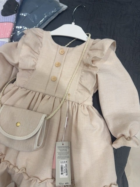 فستان بناتي بتصميم جميل مع حقيبة صغيرة مرفقة. لونه بيج ونسيجه ناعم، مثالي للمناسبات الخاصة. الأزرار الأمامية تضيف له لمسة أنيقة. متوفر بمجموعة مقاسات للأطفال.