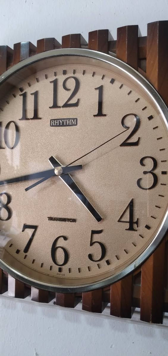 ***********
ساعة الجدارية الكلاسيكية من ريذم (Rhythm) بإطار لون خشبية ذي تصميم مضلع باللون البني.تحتوي الساعة على قرص بلون ذهبي فاتح مع أرقام عربية واضحة باللون الأسود لتسهيل القراءة.تشير الساعة إلى أنها تعمل بتقنية الترانزستور (Transistor)، مما يدل على قدم طرازها أو طابعها القديم اليابانية
