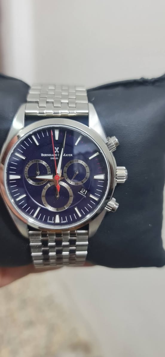 بناءً على الصورة، هذه الساعة هي من العلامة التجارية السويسرية Bernhard H. Mayer، وتحديداً موديل Ascent Chronograph (أو طراز مشابه جداً من مجموعة الكرونوغراف الكلاسيكية لديهم).
​إليك أهم مواصفاتها التقنية المعتادة لهذا الإصدار:
​المواصفات العامة:
• ​بلد المنشأ: سويسرية الصنع (Swiss Made).
• ​الهيكل (Case): مصنوع من الفولاذ المقاوم للصدأ (Stainless Steel 316L) المصقول والناعم.
• ​المينا (Dial): باللون الأزرق الداكن مع مؤشرات مضيئة (Luminescent) للساعة والدقائق.
• ​الزجاج (Crystal): زجاج ياقوت (Sapphire Crystal) مقاوم للخدش مع طبقة مضادة للانعكاس.
• ​السوار (Bracelet): سوار من المعدن (Stainless Steel) بتصميم خماسي الحلقات (أشبه بتصميم Jubilee) مع مشبك قابل للطي.
​الوظائف (Functions):
• ​نظام الحركة (Movement): كوارتز سويسري (Swiss Quartz)، وغالباً ما تستخدم هذه العلامة ماكينات Ronda.
• ​الكرونوغراف (Chronograph): تحتوي على ثلاث عدادات فرعية لقياس الثواني، الدقائق، والساعات (أو أجزاء من الثانية حسب الموديل الدقيق).
• ​التاريخ (Date): نافذة لعرض التاريخ تقع عادةً عند الساعة الرابعة أو السادسة (في صورتك تظهر عند الساعة الرابعة تقريباً).
• ​مقاومة الماء: غالباً ما تكون مقاومة للماء حتى عمق 50 أو 100 متر (5 - 10 ATM)، مما يجعلها مناسبة للاستخدام اليومي والسباحة السطحية.
​ملاحظات إضافية:.
• ​يتميز هذا الموديل بالعقرب الأحمر النحيف للثواني (الخاص بالكرونوغراف) الذي يعطي لمسة رياضية للمينا الأزرق.
​السعر ٨٥٠ الف وبيها مجال بسيط


**إذا كنت صاحب هذا الإعلان وتريد حذفه لأي سبب، رجاءا أرسل رسالة إلى الدعم الفني**