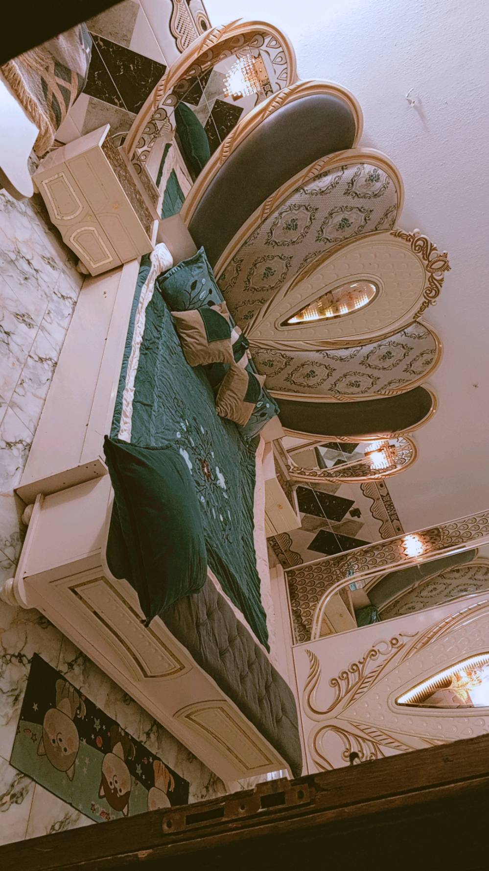 غرفة نوم مميزة بتصميم كلاسيكي فاخر، تتكون من سرير كبير ومريح مع لوح رأس ذو زخارف أنيقة ومرآة رائعة. الطقم يشمل أيضًا خزائن جانبية وتصميم فني على الجدران والخزائن. القطع مصنوعة بعناية لتضيف لمسة من الفخامة لأي غرفة نوم.