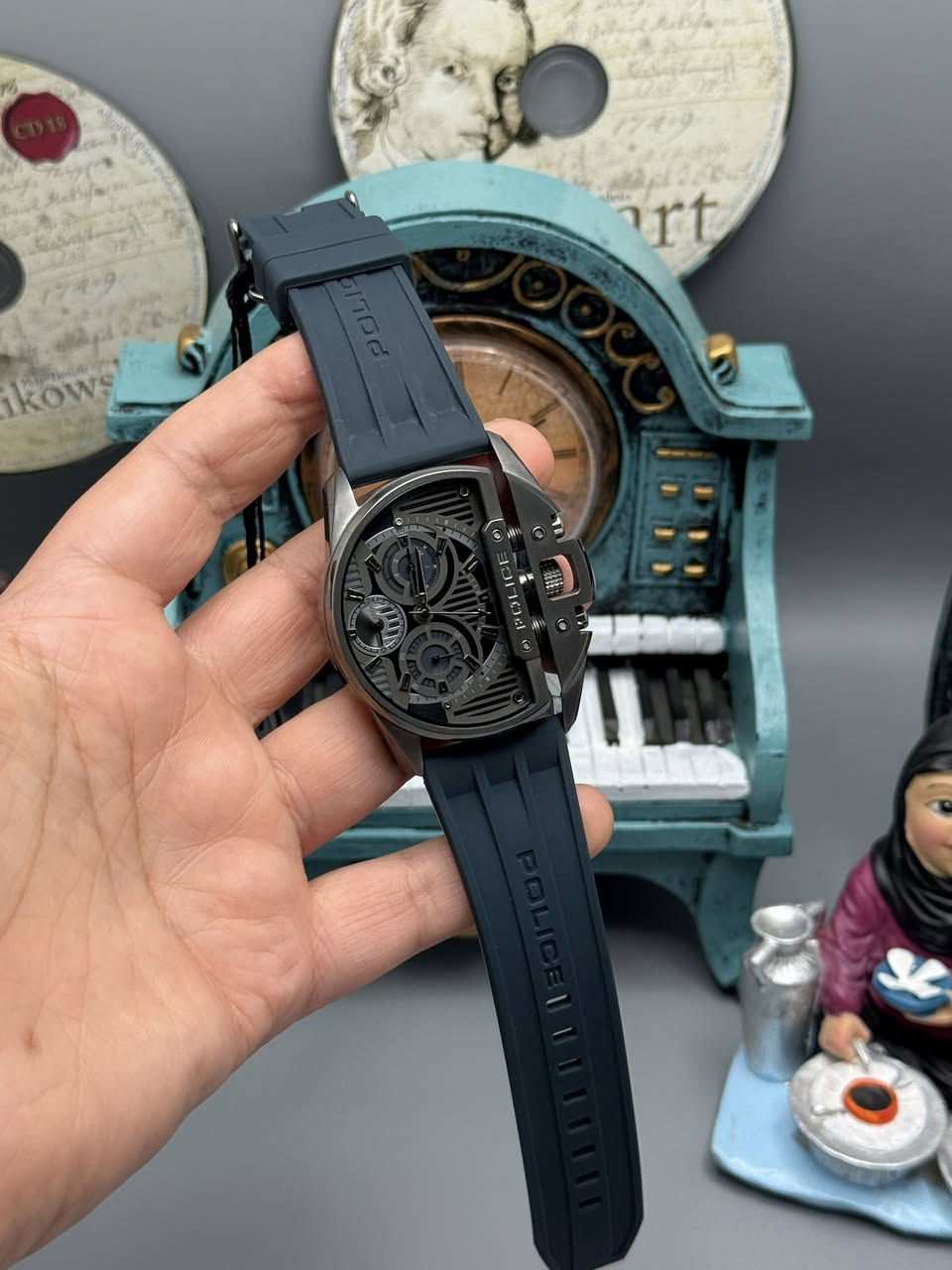 هذه الساعة هي من علامات Police التجارية، وتحديداً موديل GQ22036 (المعروف غالباً باسم سلسلة Police Luang). تتميز بتصميم "صناعي" جريء وغير تقليدي.
إليك شرح مفصل لأجزائها ومميزاتها بناءً على الصور:
1. التصميم والهيكل (The Case)
• الشكل: تأتي الساعة بتصميم "D-Shape" (على شكل حرف D)، وهو تصميم غير متماثل يعطي مظهراً قوياً على المعصم.
• المادة: الهيكل مصنوع من الفولاذ المقاوم للصدأ (Stainless Steel) المطلي باللون الرمادي الداكن أو "الرصاصي".
• غطاء التاج: نلاحظ وجود هيكل ميكانيكي ضخم يحمي "التاج" (زر الضبط) من الجانب، مثبت ببراغي وسحّابات (Springs)، مما يعزز المظهر الميكانيكي للساعة.
2. الميناء والوظائف (The Dial)
الساعة ليست مجرد ساعة عادية، بل هي ساعة Multi-Function تحتوي على عدة عدادات فرعية داخل الميناء الرئيسي:
• عداد اليوم (Day): يشير عادةً إلى أيام الأسبوع.
• عداد التاريخ (Date): لعرض يوم الشهر.
• نظام 24 ساعة: يعرض الوقت بنظام الـ 24 ساعة (ليلاً ونهاراً).
• التصميم الداخلي: الميناء "مخرم" أو يحتوي على خطوط عرضية تكشف جزءاً من الخلفية، مما يعطي عمقاً بصرياً (3D Effect).
3. الحزام (The Strap)
• المادة: الحزام مصنوع من السيليكون (أو المطاط) عالي الجودة باللون الأزرق الداكن.
• التفاصيل: نلاحظ وجود نقش حرف "P" (شعار الماركة) بشكل متكرر على الجهة الداخلية للحزام، واسم "POLICE" بارز على الجهة الخارجية، وهو مصمم ليكون مريحاً ومقاوماً للتعرق.
4. المواصفات الفنية (من خلفية الساعة)
بالنظر إلى الصورة الأولى (خلفية الساعة):
• الموديل: GQ22036.
• مقاومة الماء: مكتوب 5 ATM، وهذا يعني أنها مقاومة للماء حتى عمق 50 متراً. (مناسبة لغسل اليدين أو الأمطار أو السباحة الخفيفة، لكن لا ينصح بها للغوص العميق).
• التصميم: مسجل كـ "Copyright & Registered Design"، مما يعني أن هذا التصميم الفريد خاص بماركة بوليس فقط.
نصائح للاستخدام:
• التنسيق: الساعة ضخمة ورياضية، لذا فهي تناسب الملابس "الكاجوال" أو الملابس العصرية (Urban Style) أكثر من الملابس الرسمية الكلاسيكية.
• العناية: بما أن الحزام سيليكون، يفضل غسله بماء فاتر بعد التعرض للعرق الشديد للحفاظ على مرونته ولونه. بناءً على الكود المحفور على خلفية الساعة (GQ22036) والبحث في السجلات التقنية لشركة بوليس، إليك التفاصيل الدقيقة للموديل وسنة الإصدار:
1. اسم الموديل (Model Name)
هذا الموديل يسمى Police Daintree (بوليس دينتري).
• رقم الموديل الكامل: PEWGQ2203604 (للنسخة التي تأتي بهيكل رمادي وحزام أزرق كما في صورتك).
• كود الهيكل (Case Code): GQ22036.
2. سنة الصنع/الإصدار
• تم إصدار هذه المجموعة (Daintree) لأول مرة ضمن تشكيلة ربيع وصيف 2024 (Spring/Summer 2024).
• تعتبر هذه الساعة حديثة جداً في الأسواق، وقد تم إصدار نسخ خاصة منها (ليمتد إيديشين) تحت نفس كود الهيكل للاحتفال بالذكرى الأربعين لتأسيس العلامة التجارية بوليس (40th Anniversary).
3. معلومات إضافية عن الموديل:
• نوع المحرك (Movement): تعمل بمحرك كوارتز (بطارية) ياباني الصنع من شركة Seiko Instruments Inc (موديل المحرك: VX9N).
• المقاس: تعتبر ساعة ضخمة (Oversized) حيث يبلغ قطر الهيكل حوالي 48 ملم، مما يعطيها طابع "الدبابة" أو المظهر الصناعي القوي.
• الخامات: الهيكل من الفولاذ المقاوم للصدأ (316L) المطلي بتقنية PVD باللون الرمادي (Gunmetal).
الخلاصة:
ساعتك هي Police Daintree، وهي موديل حديث جداً من إنتاج عام 2024.

للحجز والاستفسار 
***********
