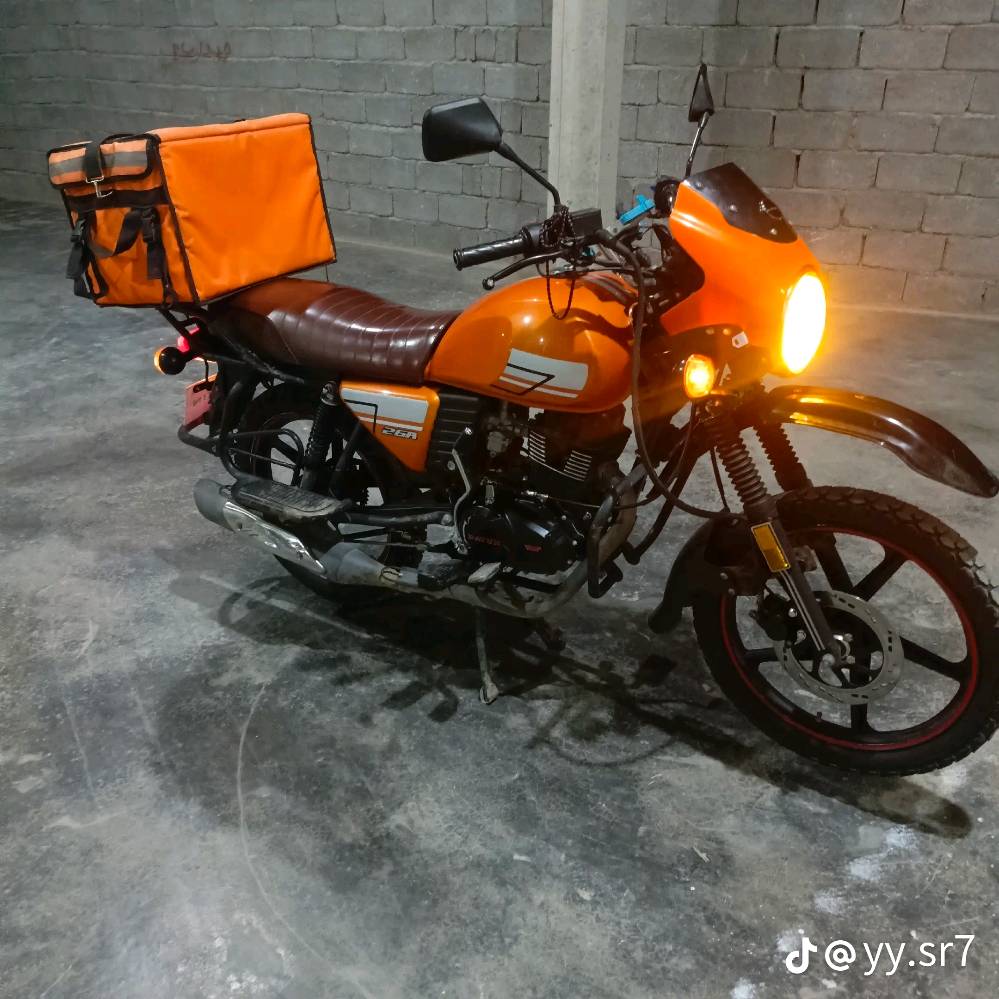 دراجة نارية برتقالية اللون بحالة جيدة جداً، مثالية للاستخدام اليومي والتنقل. تحتوي على حقيبة تخزين خلفية كبيرة، ممتازة لتوصيل الطرود أو استخدامات المتعددة. تمتاز بمقعد مريح وتصميم عصري. السعر منافس ومناسب لمن يبحث عن أداء عالي بأسعار معقولة.