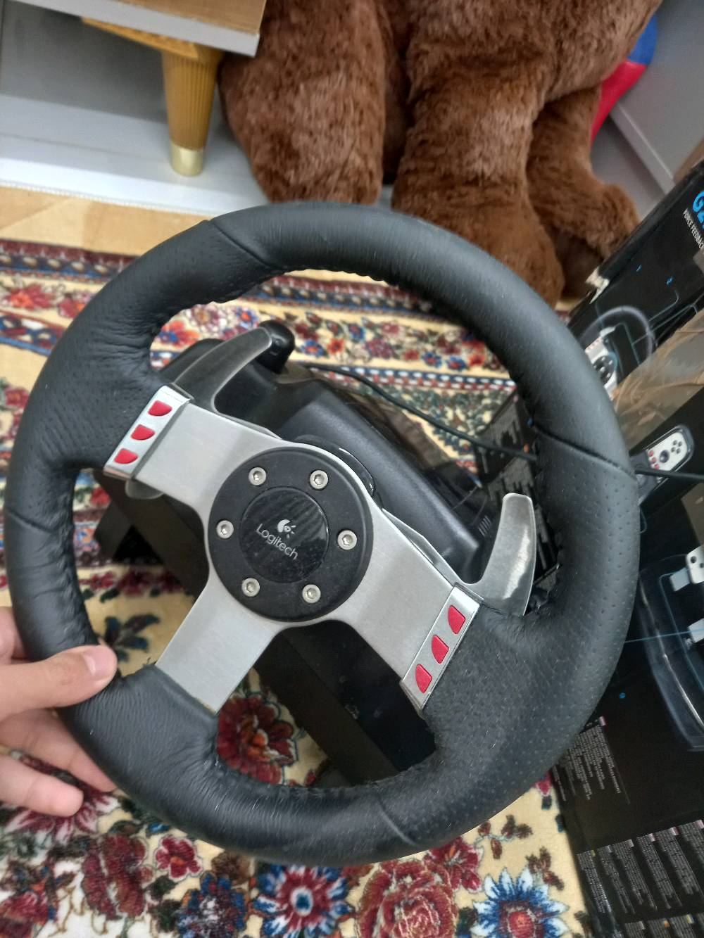 📍بغداد-الدوره-ابودشير-شارع جامع الرحمان

🔴مواصفات🔴 
🎮 المواصفات الأساسية لـ Logitech G27
زاوية دوران الدركسون: حتى 900 درجة (مثل السيارة الحقيقية). �
Wikipedia
نظام Force Feedback: محركين يعطون إحساس واقعي بالطريق والاهتزاز. �
B&H Photo Video
عدد الدواسات: 3 دواسات (بنزين – فرامل – كلتش). �
Wikipedia
القير:
قير يدوي 6 سرعات (H-Pattern)
مع Paddle Shifters خلف الدركسون. �
Wikipedia
المواد:
الدركسون مكسو جلد حقيقي
الدواسات معدنية (Steel). �
B&H Photo Video
الأزرار: حوالي 16 زر قابل للبرمجة + D-Pad. �
B&H Photo Video
الإضاءة: لمبات RPM لمعرفة وقت تغيير القير. �
B&H Photo Video
التوصيل: USB سلكي. �
support.logi.com