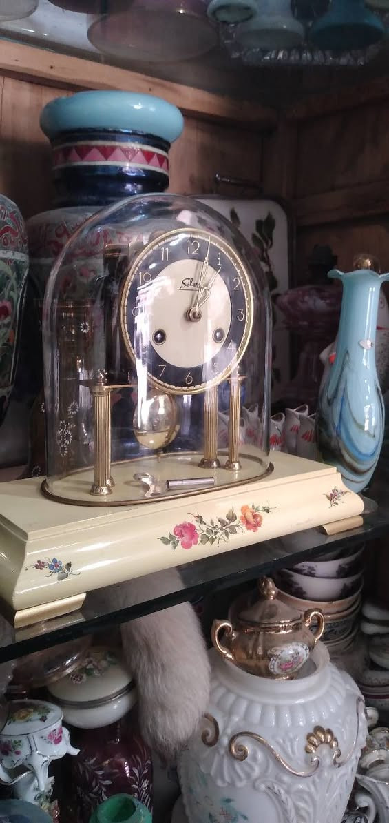 ساعة مكتبية أو رفّية (Mantel/Table Clock) كلاسيكية مميزة.  
​العلامة التجارية:   اسم الساعه "Selva"، وهي علامة تجارية ألمانية معروفة جداً في مجال قطع غيار الساعات، ومجموعات تركيب الساعات، والساعات الميكانيكية التقليدية بجودة عالية.
​المنشأ:  أسفل الرقم 6 عبارة صغيرة  مكتوب "Made in Germany" (صنع في ألمانيا)، وهو أمر متوافق تماماً مع العلامة التجارية Selva.
​ التصميم والهيكل
​القبة الزجاجية (Glass Dome): الساعة مغطاة بقبة زجاجية شفافة منحنية (تُعرف بساعات القبة أو ساعات الذكرى السنوية أحياناً، وإن كانت هذه تعمل ببندول تقليدي وليس بندولاً دواراً). وظيفتها حماية الآلية الداخلية والميناء من الأتربة.
​الميناء (Dial): يتميز بتصميم ثنائي اللون (حلقة خارجية سوداء تحتوي على أرقام عربية مذهبة واضحة، ومركز دائري بلون كريمي/أبيض مطفأ).
​الأعمدة والقاعدة: ترتكز الساعة على أعمدة نحاسية مضلعة مذهبة فوق قاعدة بيضاء أو كريمية المزينة بنقوش وردية ناعمة مرسومة باليد، مما يعطيها طابعاً أنثوياً أو ريفياً كلاسيكياً (Shabby Chic / Vintage style).
​الآلية والتشغيل (الميكانيكا)
​المفاتيح وثقوب التعبئة: يحتوي الميناء على ثقبين للتعبئة (Winding holes) بجانب الرقمين 4 و 8. هذا يعني أن الساعة تحتوي على نابضين (زُنبركين): واحد لتشغيل حركة عقارب الساعة، والآخر مخصص لآلية الرنين (الدق أو الجرس).
​مفتاح التعبئة:  مفتاح التعبئة المعدني الأصلي مستلقياً على قاعدة الساعة داخل القبة الزجاجية.
​البندول (Pendulum): بندول نحاسي لامع أسفل الميناء، وهو المسؤول عن تنظيم الوقت عبر حركته الاهتزازية يميناً ويساراً.
​ الحالة العامة  الساعة في حالة جيدة جداً ونظيفة. النحاس يحتفظ بلمعانه، والزجاج سليم لا تظهر فيه شروخ واضحة، والرسومات على القاعدة بحالة ممتازة.
​القيمة: هذا النوع من الساعات يجمع بين القيمة الوظيفية والجمالية كقطع ديكور "أنتيك" أو عتيقة مرغوبة لمحبي الساعات الألمانية الميكانيكية.


**إذا كنت صاحب هذا الإعلان وتريد حذفه لأي سبب، رجاءا أرسل رسالة إلى الدعم الفني**