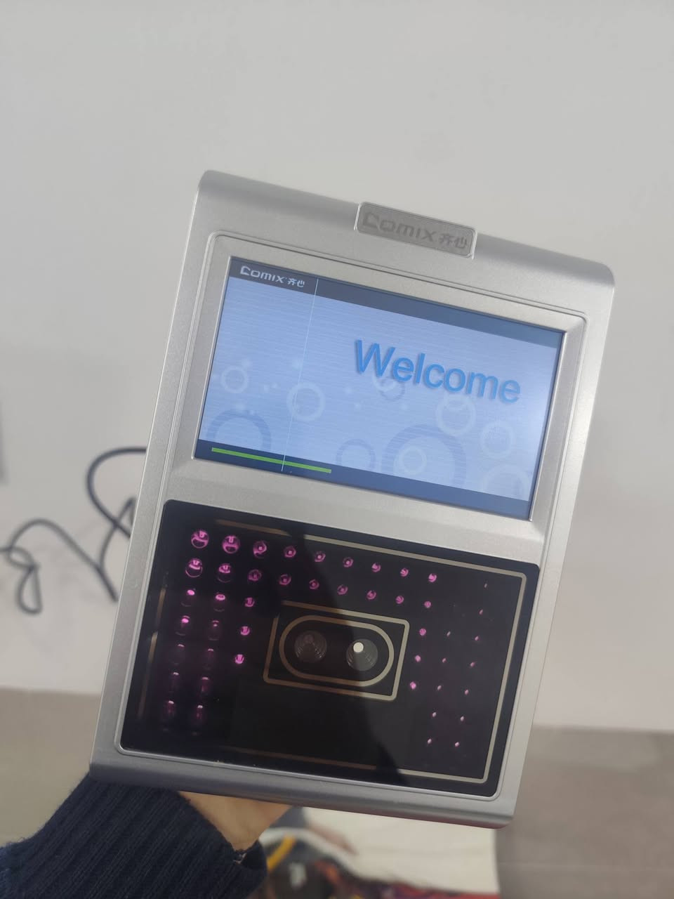 ا الجهاز هو جهاز بصمة الوجه (Face Recognition Terminal) من ماركة Comix، وهو مخصص لإدارة الحضور والانصراف للموظفين أو للتحكم في الدخول (Access Control).
إليك التفاصيل التقنية والوظائف بناءً على الصور المرفقة:
1. الوظائف الأساسية للجهاز
التعرف على الوجه: يستخدم الكاميرات المزدوجة والحساسات الضوئية (المصابيح الأرجوانية الظاهرة في الصور) للتعرف على ملامح الوجه بدقة، حتى في الإضاءة المنخفضة.
تسجيل الحضور والانصراف: يتيح للموظفين تسجيل وقت الدخول والخروج بمجرد الوقوف أمام الجهاز.
إدارة البيانات: يحتوي على قائمة "Report" لاستخراج تقارير الحضور مباشرة، وقائمة "Schedule" لضبط مواعيد العمل والنوبات.
2. المواصفات الظاهرة
الشاشة: شاشة ملونة تعمل باللمس لعرض القوائم والتعليمات.
المنافذ الجانبية:
USB: لسحب التقارير على "فلاش ميموري" أو تحديث النظام.
Mini USB: للاتصال المباشر بالكمبيوتر.
فتحة الطاقة: لتوصيل المحول الكهربائي (5 فولت غالباً).
زر Reset: لإعادة تشغيل الجهاز في حال حدوث تعليق.
3. شرح أيقونات القائمة الرئيسية
كما يظهر في الصورة الثالثة:
User: لإضافة موظف جديد، التقاط صورته، أو تعديل بياناته.
Schedule: لضبط ساعات العمل الرسمية والعطلات.
Report: لاستخراج جداول الحضور بصيغة Excel.
System: لضبط الوقت والتاريخ، اللغة، وإعدادات الشبكة.
Bell: لضبط تنبيهات صوتية (جرس) في أوقات معينة.
User Info: لعرض سجلات الموظفين المسجلين حالياً.


**إذا كنت صاحب هذا الإعلان وتريد حذفه لأي سبب، رجاءا أرسل رسالة إلى الدعم الفني**