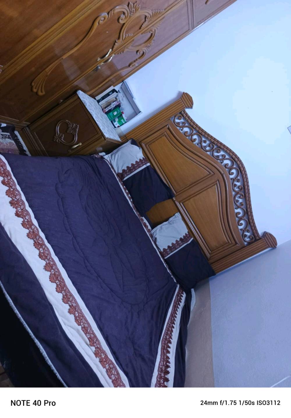 غرفة نوم خشبية أنيقة تتضمن دولاب كبير بتصميم مزخرف وسرير مزدوج مع كومودينة. الخشب مصقول وذو جودة عالية، والزخارف تضيف لمسة كلاسيكية للمكان. يناسب الغرفة الرئيسية ويضيف لمسة من الفخامة والراحة.