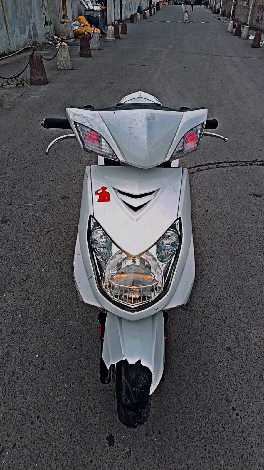 دراجة نارية نوع سكوتر لون أبيض بحالة جيدة، مثالية للتنقل داخل المدينة. تصميمها أنيق ومزودة بأضواء أمامية ساطعة لسهولة القيادة في الليل. مناسبة للي يبحث عن وسيلة نقل اقتصادية وعملية.