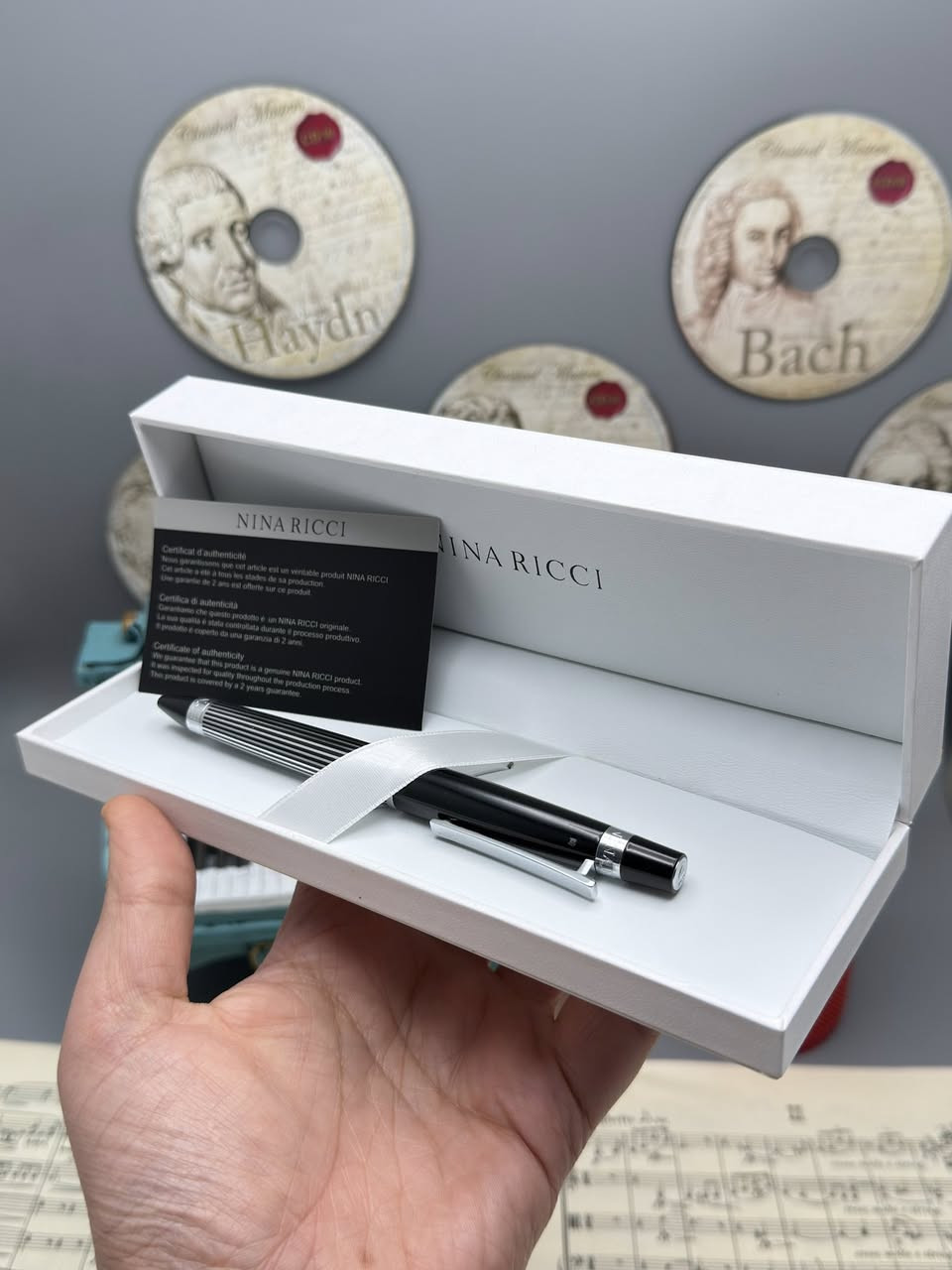 نينا ريتشي (Nina Ricci). هذه الأقلام تُعرف بكونها إكسسوارات فاخرة تجمع بين الأناقة الباريسية والعملية.
إليك شرح مفصل لما تظهره الصور:
1. العلامة التجارية والجودة
• الماركة: Nina Ricci هي دار أزياء راقية، وأقلامها تُصنف كأدوات كتابة "برستيج" (Prestige).
• الأصالة: يظهر في الصور "شهادة أصالة" (Certificate of Authenticity)، مما يؤكد أن القلم أصلي ويأتي مع ضمان (غالباً لمدة سنتين ضد عيوب التصنيع).
2. التصاميم والموديلات الظاهرة
من خلال الصور، نرى أربعة أشكال مختلفة، مما يوفر خيارات متنوعة للأذواق:
• القلم الأول (بني مموج): يتميز بنقشة "Tortoise" أو التورتويز (صدفة السلحفاة) الكلاسيكية مع لمسات معدنية داكنة. هذا التصميم يوحي بالفخامة التقليدية والمظهر الدافئ.
• القلم الثاني (أسود وفضي): تصميم كلاسيكي "مينيماليست" باللون الأسود اللامع مع حواف فضية، وهو مثالي لرجال الأعمال والمناسبات الرسمية.
• القلم الثالث (ذهبي مخطط): قلم باللون الذهبي الكامل مع خطوط طولية محفورة، يعطي طابعاً ملكياً لافتاً للنظر.
• القلم الرابع (فضي/كروم مخطط): مشابه للذهبي ولكن باللون الفضي، يتميز بالهدوء والعصرية، ومقاوم بشكل جيد للخدوش بفضل المادة المعدنية.
3. المواصفات الفنية
• نوع القلم: يظهر من الرؤوس أنها أقلام حبر جاف (Ballpoint) تعمل غالباً بآلية التدوير (Twist mechanism) لفتح وإغلاق القلم.
• الخامات: الهيكل عادة ما يكون مصنوعاً من النحاس المطلي بالروديوم، الذهب، أو الورنيش عالي الجودة (Lacquer).
• التغليف: يأتي في علبة بيضاء فاخرة مبطنة من الداخل بكلمة "NINA RICCI" مطبوعة بشكل أنيق، مما يجعله خياراً ممتازاً للهدايا.
4. مميزات الاقتناء
• الوزن: هذه الأقلام تمتاز بوزن متزن (ليست خفيفة جداً ولا ثقيلة)، مما يوفر راحة أثناء الكتابة الطويلة.
• سهولة التعبئة: تستخدم عبوات حبر قياسية متوفرة بسهولة في المكتبات الكبرى.
• القيمة: يعتبر قطعة إكسسوار تكمل المظهر الشخصي، تماماً مثل الساعة أو المحفظة.

للحجز والاستفسار 
***********

