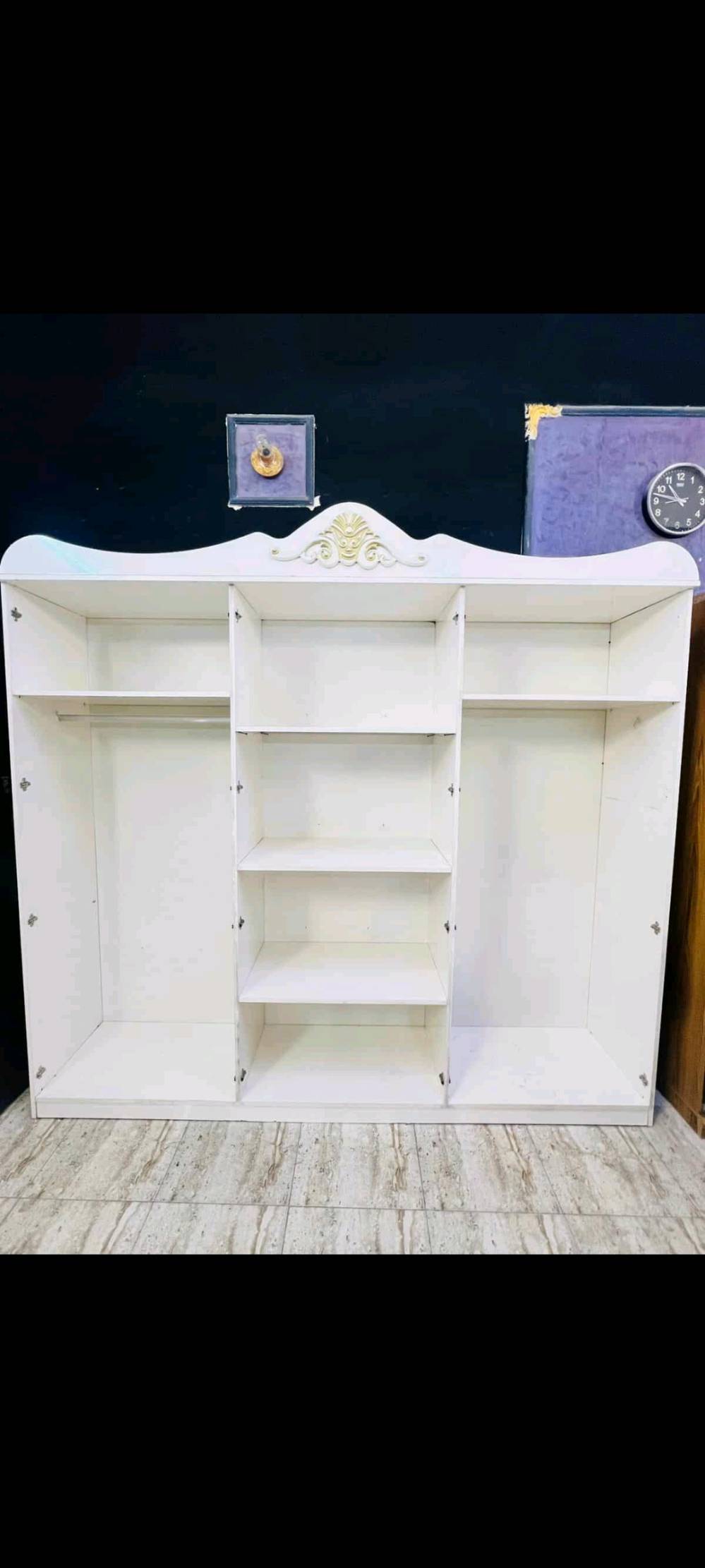 غرفة نوم فاخرة بتصميم كلاسيكي تشمل سرير مريح مع لوح أمامي مبطن باللون الأزرق الداكن وخزانة ملابس كبيرة مع مرايا زخرفية. تتميز الغرفة بتفاصيل ذهبية على الأبواب والأدراج، مما يضفي لمسة من الفخامة والرقي. الطقم يشمل أيضًا تسريحة مع مرآة كبيرة وكرسي مبطن لتوفير الراحة أثناء التحضير اليومي. الأثاث مصنوع بجودة عالية ويضفي لمسة فنية على أي غرفة نوم.