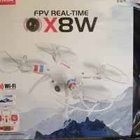 الصورة طائرة درون من نوع Syma X8W، وهي طائرة رباعية المراوح (Quadcopte...