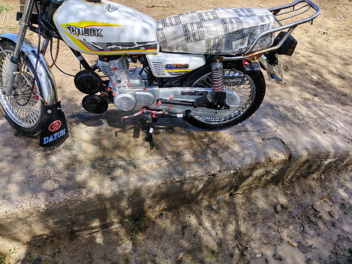 دراجة نارية نوع دايون CG125 بحالة ممتازة، لونها أبيض مع رسومات جانبية. الدراجة نظيفة ومجهزة بالكامل، مما يجعلها مثالية للاستخدام اليومي أو المشاوير الطويلة.