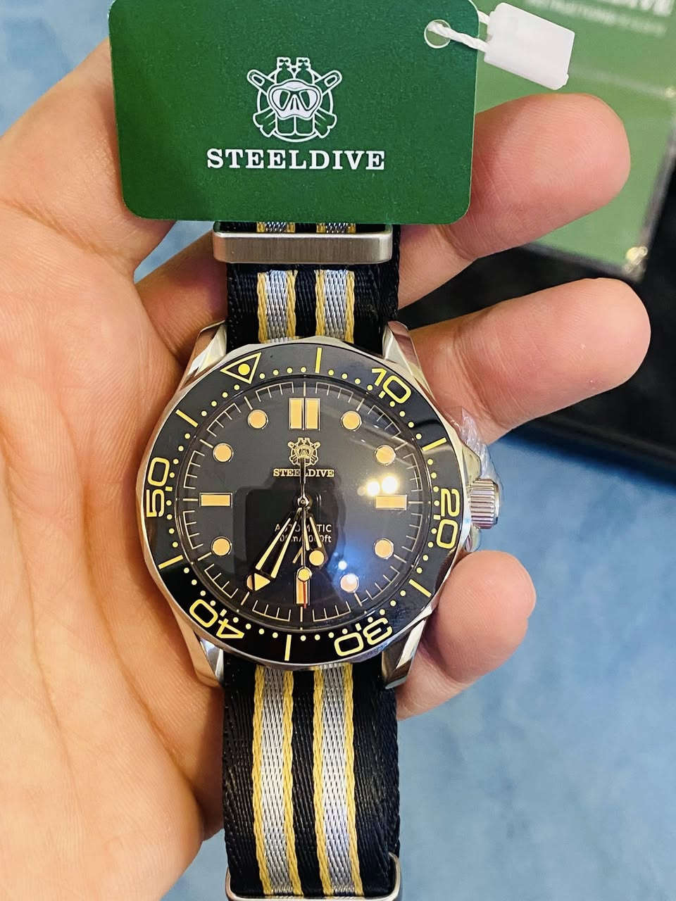 هذه الساعة هي Steeldive SD1957، وهي ساعة غوص أوتوماتيكية تُعتبر "Homage" (ساعة مستوحاة في تصميمها) لساعة أوميغا الشهيرة "No Time To Die"

أبرز مواصفات هذه الساعة:
* الحركة: تعمل بحركة أوتوماتيكية من نوع Seiko NH35 التي تدعم خاصية التعبئة اليدوية وإيقاف الثواني (Hacking).��
* مقاومة الماء: تصل قدرتها على مقاومة الماء إلى 300 متر. ��
* الزجاج: تأتي بزجاج من كريستال الياقوت (Sapphire Crystal) المطلي بطبقة مضادة للانعكاس. ��
* الهيكل والقياس: يبلغ قطر الهيكل 42 ملم، وهو مصنوع من الفولاذ المقاوم للصدأ. ��
* الإضاءة: تتميز بمادة Swiss C3 Super-LumiNovaالمضيئة على العقارب ومؤشرات الميناء لرؤية واضحة في الظلام.


**إذا كنت صاحب هذا الإعلان وتريد حذفه لأي سبب، رجاءا أرسل رسالة إلى الدعم الفني**