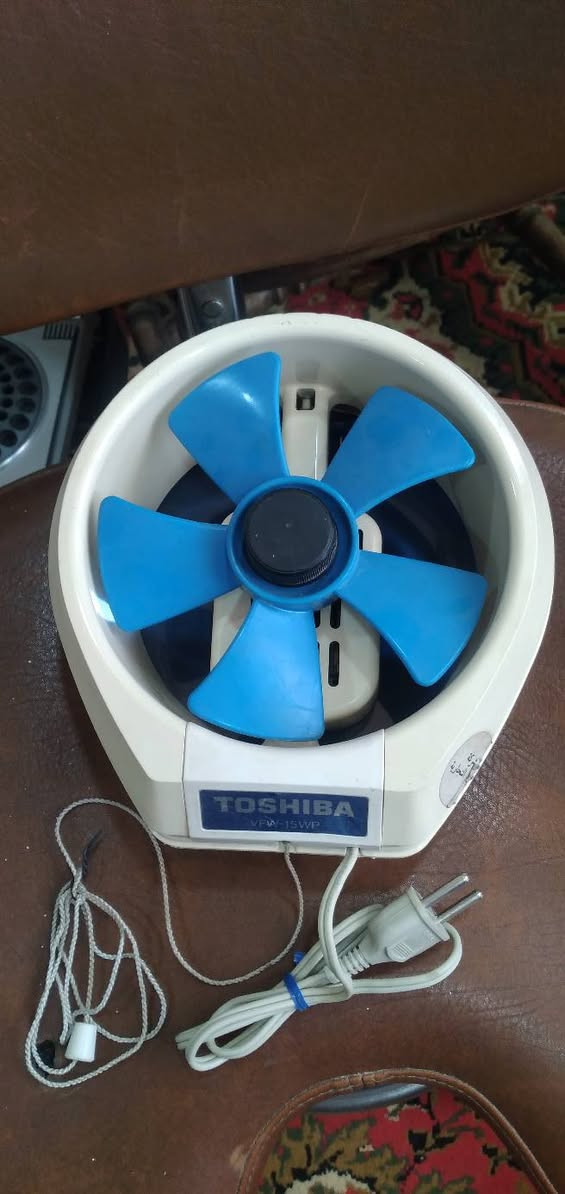 ***********
مروحة تهوية (شفاط) من نوع توشيبا (Toshiba)، وتتميز بتصميمها الكلاسيكي المتين الذي يركز على الكفاءة التشغيلية المباشرة.
​العلامة التجارية: توشيبا (Toshiba)
​الموديل: VFW-15WP.
​التصميم: مروحة شفط جدارية صغيرة الحجم، عادة ما تُستخدم في المطابخ أو الحمامات لتجديد الهواء.
​المكونات: 
​الشفرات: تحتوي على 5 ريش بلاستيكية باللون الأزرق، مصممة بتناظر لتوفير تدفق هواء هادئ ومنتظم.
​الهيكل: إطار بلاستيكي بلون كريمي/أبيض مائل للصفرة، وهو نمط شائع في الأجهزة اليابانية الكلاسيكية.
​نظام التشغيل: سلك سحب (Pull Cord) للتشغيل والإيقاف، وهو نظام ميكانيكي بسيط وعملي.
​التوصيل: سلك كهربائي ثنائي الرأس (Plug).
​الاستخدام والتركيب:
​هذا الموديل مخصص للتركيب داخل فتحات دائرية في الجدران أو النوافذ.
​يُعرف هذا النوع من إنتاج توشيبا بالاعتمادية العالية وطول العمر الافتراضي للمحرك، وهو ما يتماشى مع الاهتمام بالصناعات والمعدات ذات الطابع الفني والهندسي المتين.
​ بلد المنشأ اليابان ،
