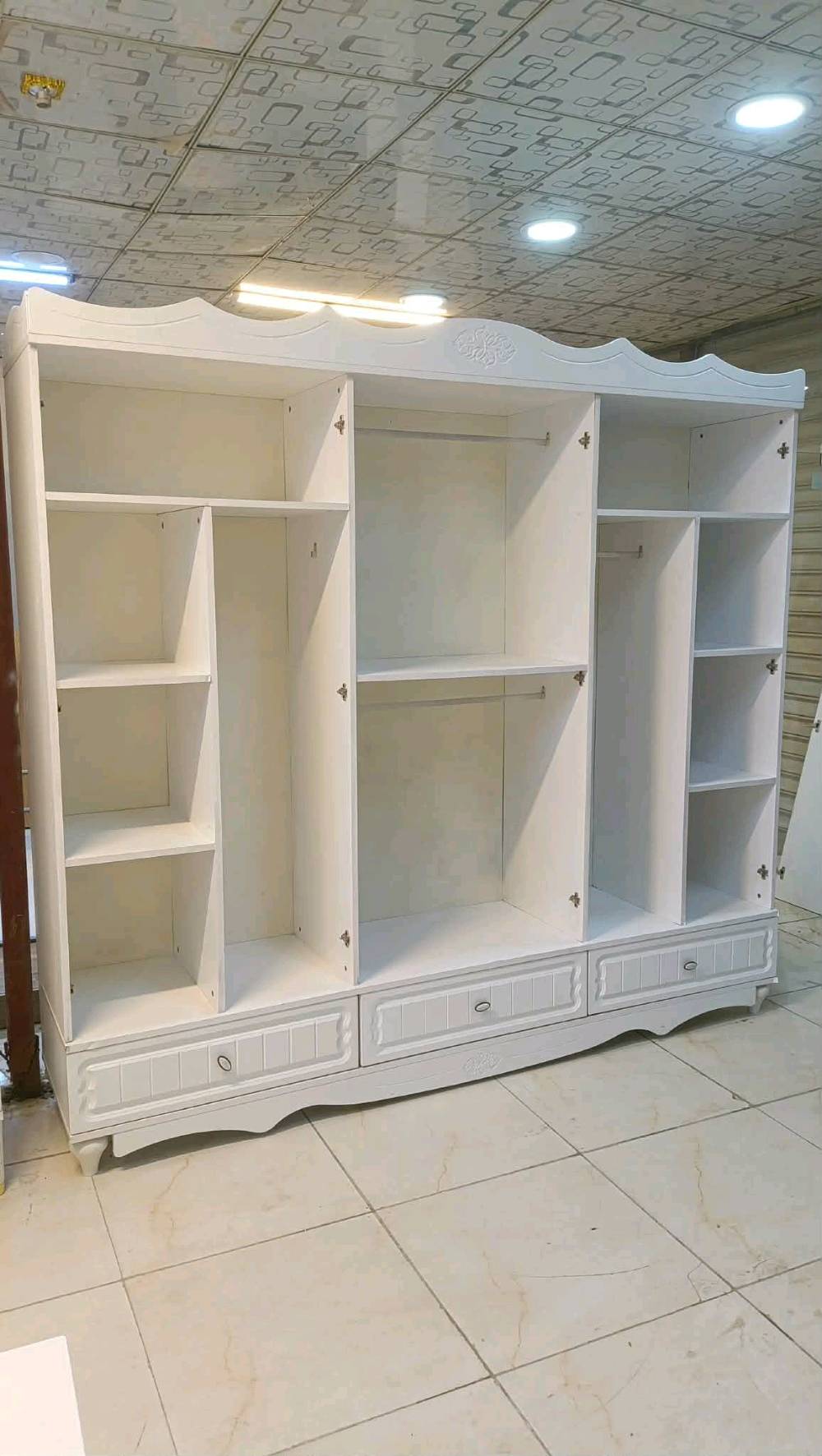 مجموعة غرف نوم بيضاء أنيقة وعصرية، تشمل خزانة ملابس كبيرة مزودة بأبواب مرآة، مع تسريحة وأدراج متعددة للتخزين، وسريران بتصميم ظهر مرتفع منجد بجلد فاخر. تناسب عوائل تبحث عن لمسة من البساطة والجمال في غرفة النوم.