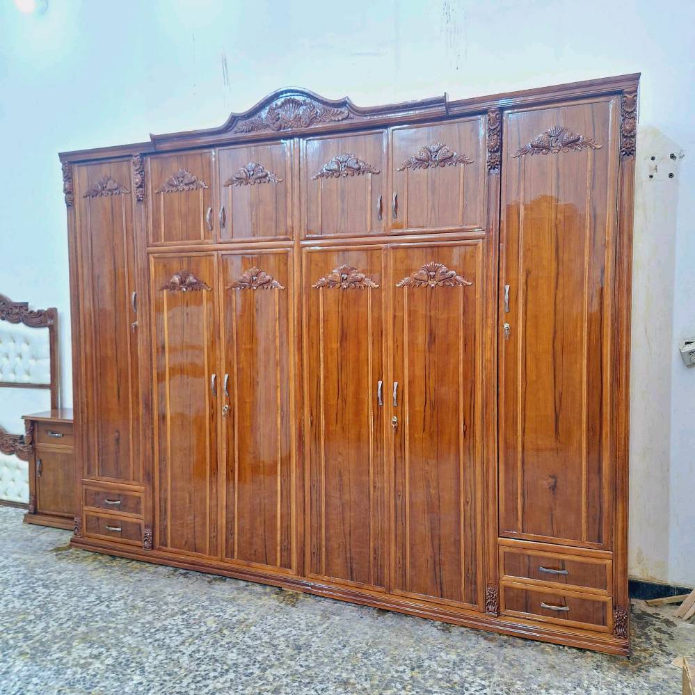 الغرفة المعروضة تتكون من سرير ملكي مع تفصيلات فخمة وزخارف خشبية أنيقة، بالإضافة إلى دولاب ضخم بأبواب متعددة ومرآة كبيرة تضيف لمسة كلاسيكية للغرفة. التصميم متكامل ويحتوي على كومودينات وأماكن تخزين متعددة. مثالية لمن يبحث عن ديكور راقي وعملي في نفس الوقت.