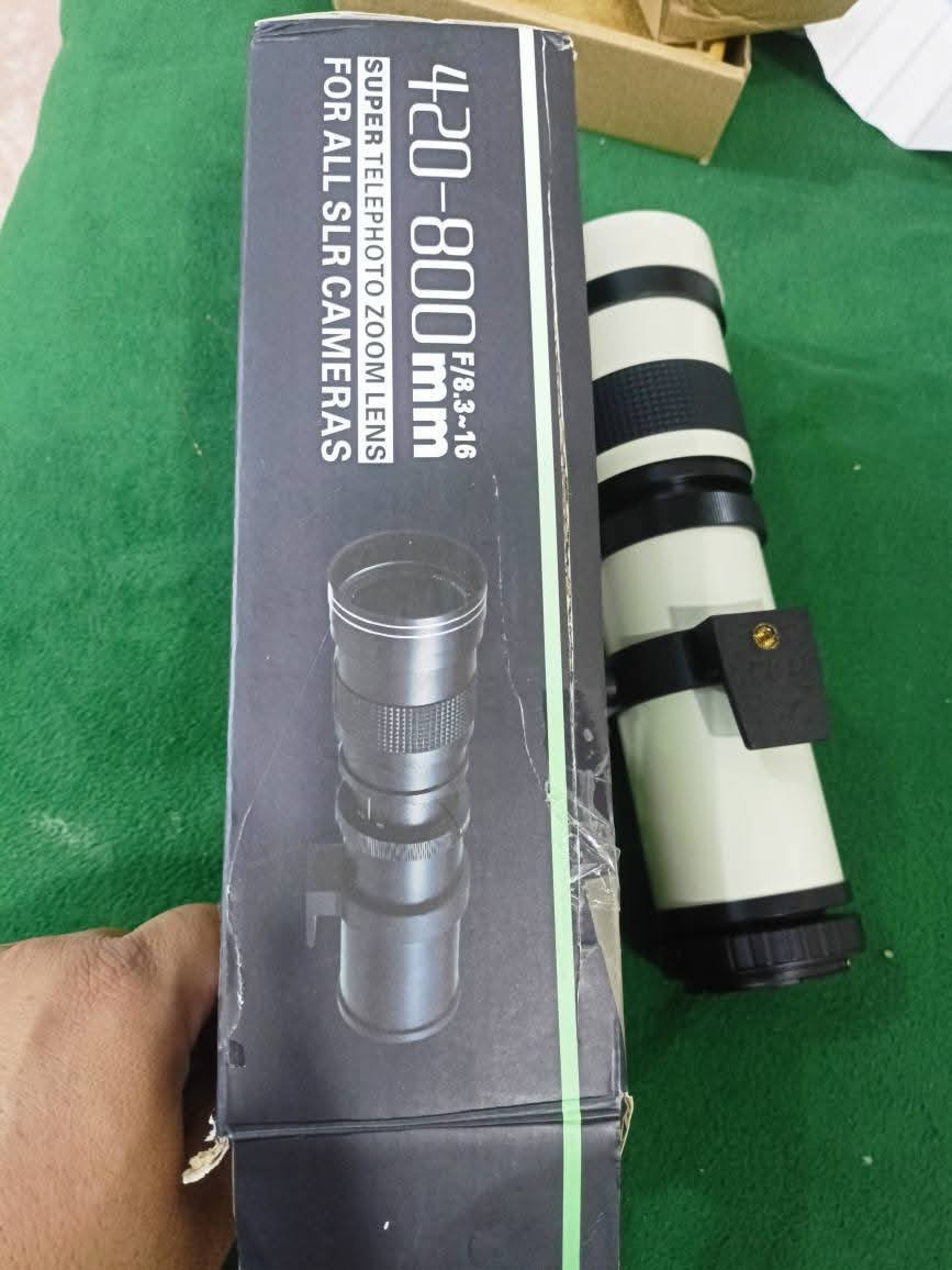 المنتج المعروض هو عدسة تكبير مقربة يدوية فائقة (Super Telephoto Manual Zoom Lens) بمدى بؤري يتراوح بين 420 و 800 ملم وفتحة عدسة F/8.3-16، متوافقة مع كاميرات SLR وDSLR المختلفة.
معلومات المنتج والميزات الرئيسية

النوع: عدسة تكبير (زووم) مقربة فائقة بتركيز يدوي (MF).

المدى البؤري: 420-800 ملم.

فتحة العدسة: F/8.3 عند 420 ملم، وتتغير تلقائياً إلى F/16 عند 800 ملم.

التوافق: مصممة للاستخدام مع محول T-mount، مما يجعلها متوافقة مع مجموعة واسعة من الكاميرات مثل Canon و Nikon و Sony و Pentax وغيرها من موديلات SLR و DSLR.

البناء البصري: تتضمن تصميمًا بصريًا متعدد الطبقات ومشتتًا منخفضًا للزجاج البصري لضمان صور عالية الجودة وتقليل التوهج.

التصميم: تتميز بهيكل قوي من سبائك الألومنيوم.

الاستخدام: مثالية لتصوير الحياة البرية، والرياضة، والمناظر الطبيعية البعيدة، والقمر، وغيرها من الأهداف البعيدة.

الملحقات: تأتي عادةً مع غطاء أمامي وخلفي، وحقيبة حمل ناعمة، وحلقة محول T-mount (مثل T2-Nikon الظاهرة في الصورة). 

ملاحظات هامة

هذه العدسة تعمل بوضع التركيز اليدوي فقط ولا تحتوي على اتصالات إلكترونية أو تركيز تلقائي (AF).

قد تعرض الكاميرا رسالة "العدسة غير متصلة" (lens not attached)، وفي هذه الحالة يجب ضبط إعدادات الكاميرا للسماح بالتقاط الصور بدون عدسة أو استخدام وضع M اليدوي بالكامل.
الي يحتاجه متواجد خاص واتساب مازنجر ***********
