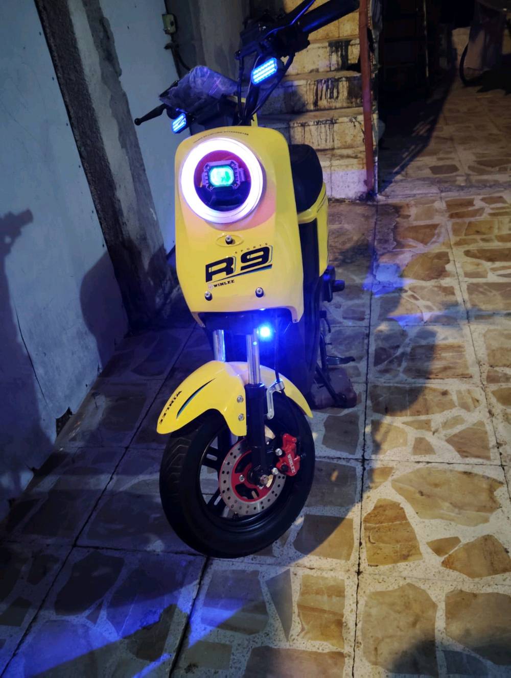 دراجة كهربائية بارزة بلون أصفر وجريء مع طراز R9. مزودة بإضاءة LED أمامية وخلفية لإضاءة الطريق في الليل. تعتبر الدراجة بحالة ممتازة مع البطارية مشحونة بالكامل وجاهزة للاستخدام. مناسبة للتنقل اليومي في المدينة بطريقة سهلة وسريعة واقتصادية.