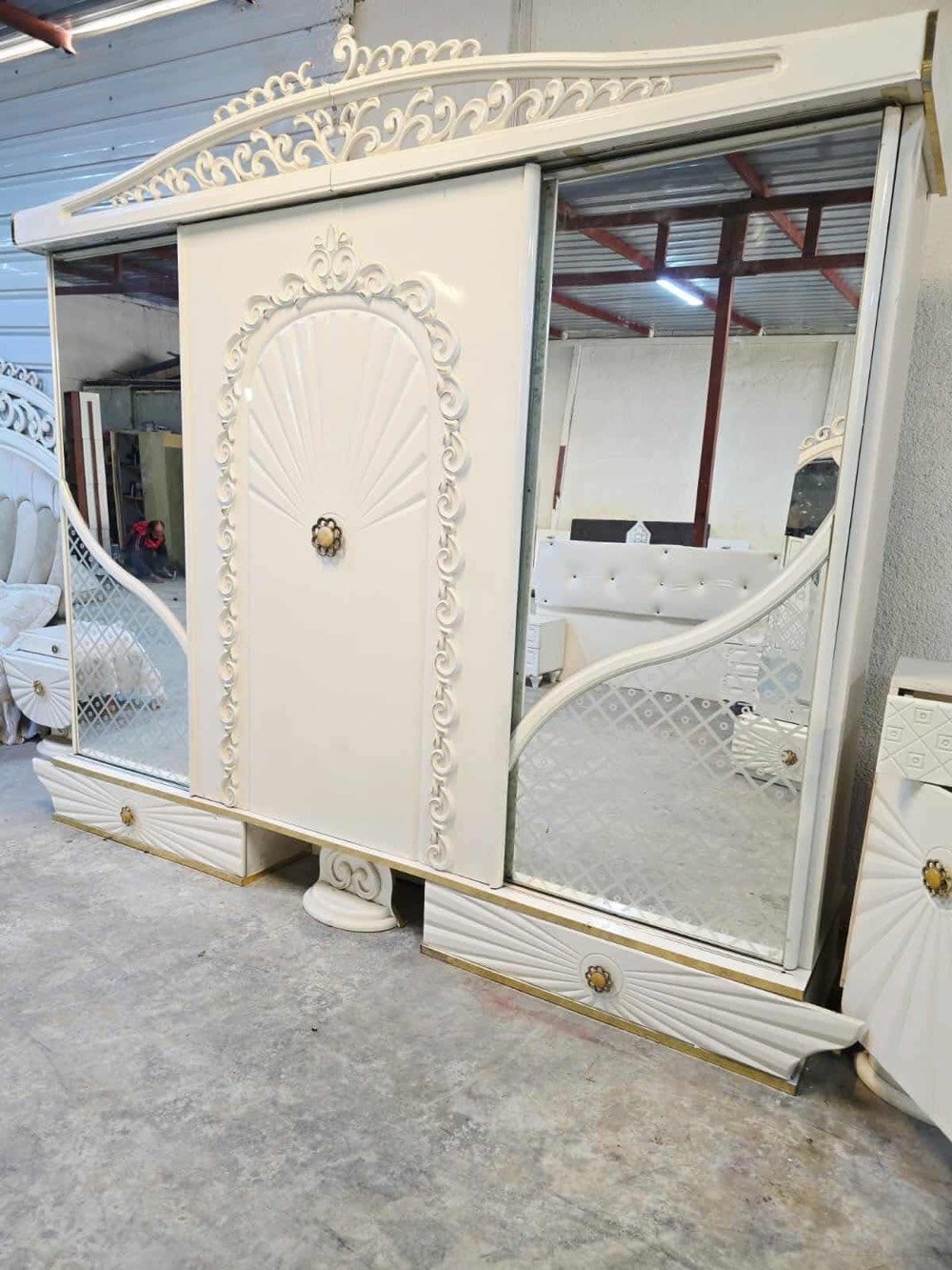 غرفة نوم فاخرة تصميم كلاسيكي، تتضمن سرير كبير مع خلفية منجدة بتفاصيل زخرفية جذابة باللون الأبيض، بالإضافة إلى خزانة ملابس مرايا وشيفونيرة مع أدراج واسعة. التصميم يتميز بالنقوش الكلاسيكية التي تضيف لمسة من الأناقة والرقي للغرفة. الأثاث بحالة جيدة ويضفي لمسة فاخرة على أي غرفة النوم.