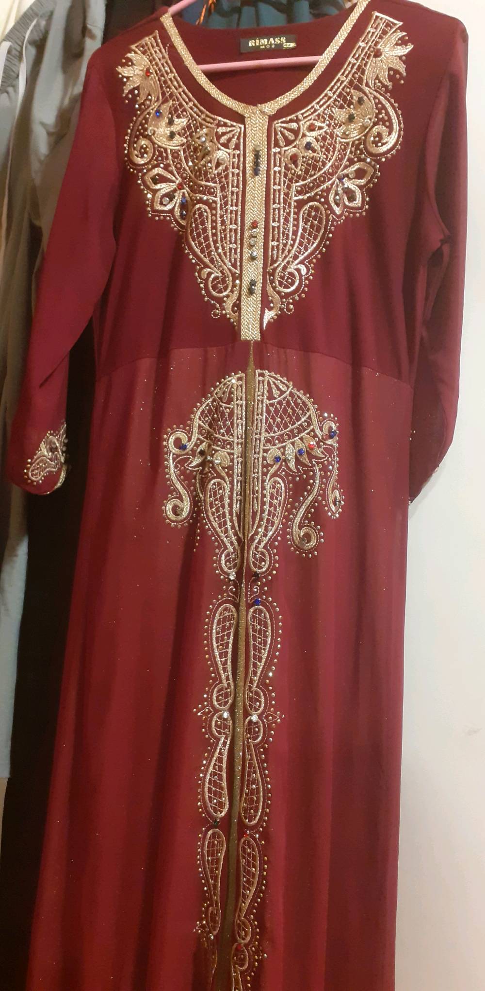 هذا قفطان أنيق بلون خمري مع تطريزات ذهبية بارزة وأحجار متعددة الألوان. مثالي للمناسبات الخاصة وحفلات الزفاف. القفطان يتميز بتصميمه الفريد والتفاصيل الدقيقة التي تضيف لمسة من الأناقة والجمال.