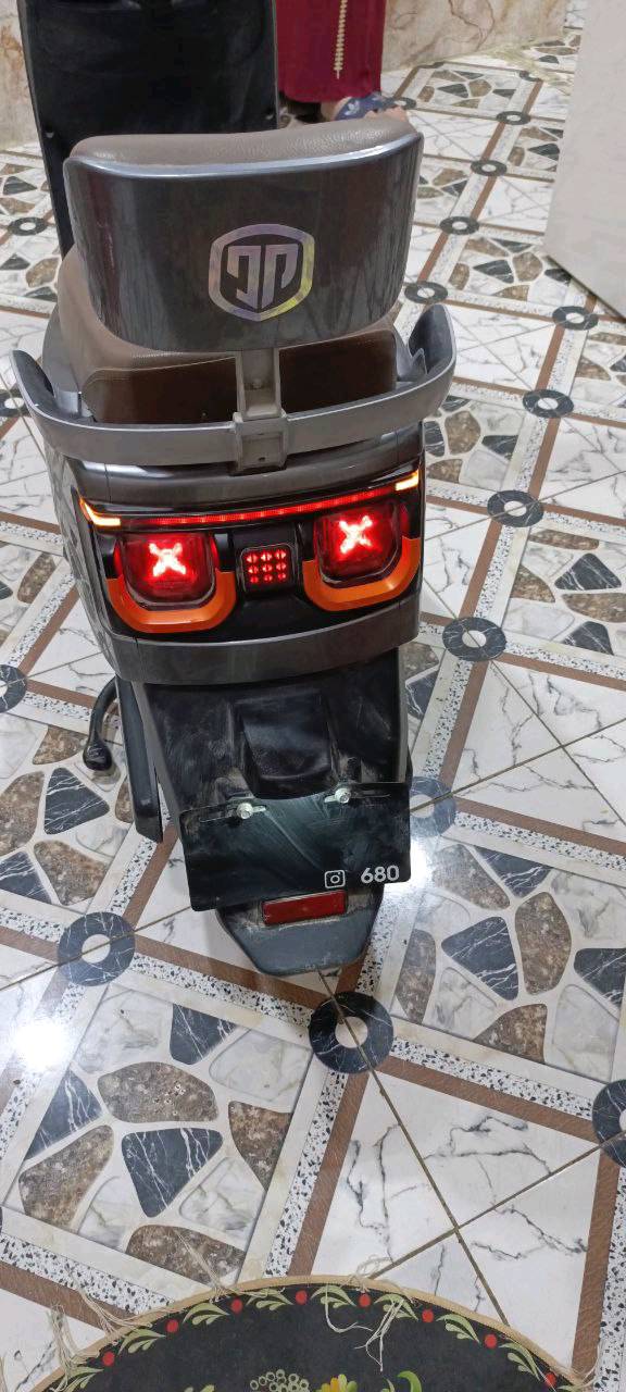 دراجة نارية كهربائية حديثة، بحالة جيدة جداً، لونها رمادي مع تفاصيل برتقالية مميزة. تحتوي على بطارية قوية لتوفير تجربة قيادة سلسة واقتصادية. مناسبة للتنقل اليومي داخل المدينة.