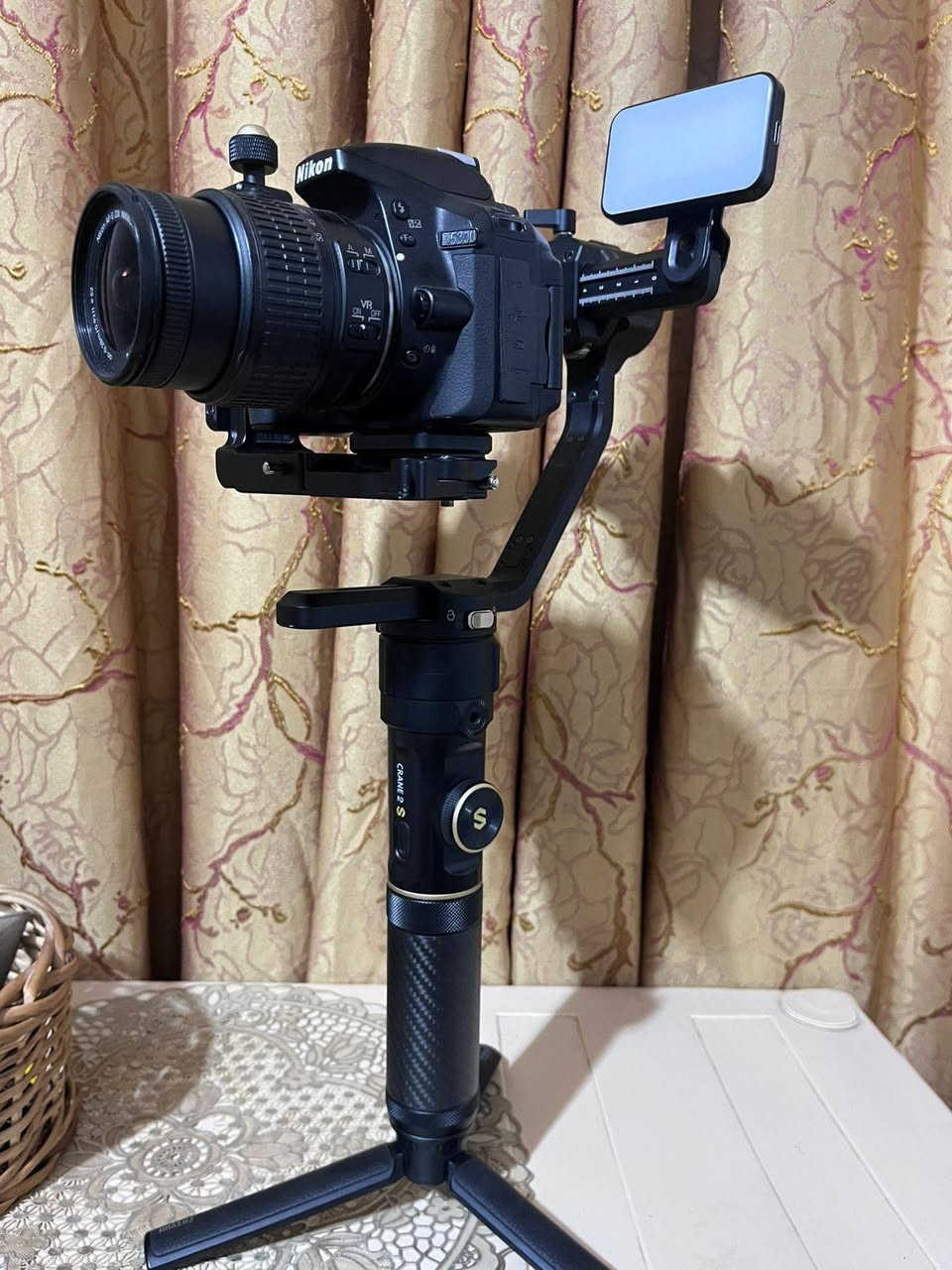 1. الكاميرا والعدسة (Body & Lens)
نوع الكاميرا: Nikon D5300 (كاميرا احترافية من فئة DSLR معروفة جداً بموثوقيتها).
 دقة وميزات الكاميرا:
 مستشعر بدقة 24.2 ميجابكسل يعطي صوراً عالية الدقة وتفاصيل حادة.
 شاشة خلفية متحركة (تفتح وتفتر) وهي ممتازة جداً لتصوير الفيديو والـ Vlogs أو السيلفي.
 دعم تصوير فيديو بدقة Full HD (1080p) بسرعة تصل إلى 60 إطار في الثانية، مما يعطي سلاومة ونعومة بالفيديو.
 تحتوي على Wi-Fi مدمج لنقل الصور مباشرة للموبايل.
 العدسة (Lens): عدسة نيكون الأساسية AF-S NIKKOR 18-55mm f/3.5-5.6G VR.
 ميزة الزووم: مثل ما ذكرتِ، الصورة تتكبر وتتصغر (من 18mm للقطات الواسعة إلى 55mm للقطات القريبة والبورتريه).
 مانع اهتزاز (VR): العدسة مجهزة بنظام تقليل الاهتزاز الاهتزاز البصري لضمان صور واضحة بدون غواش حتى أثناء الحركة.
2. مانع الاهتزاز الاحترافي (Gimbal)
 النوع الموديل: Zhiyun Crane 2S (واضح من الشعار المكتوب باللون الذهبي والكتابة على يد المانع).
 وظيفة الجهاز: هذا الجهاز مخصص للمصورين وصناع المحتوى المحترفين؛ حيث يوازن الكاميرا تماماً ويمنع أي اهتزاز أثناء المشي أو الركض، ليظهر الفيديو ناعماً وسلساً مثل تصوير الأفلام السينمائية.
 المميزات الظاهرة بالصور:
 يد كربون فايبر (Carbon Fiber) خفيفة وقوية.
 أقفال أمان للمحاور (Axis Locks) تسهل عملية الموازنة والتنقل (كما في ⁠image.png⁠ و ⁠image_6.png⁠).
 قاعدة ترايبود (Tripod) سفلية صغيرة لثبات المانع على الأسطح.
3. الملحقات الإضافية (Accessories)
 إضاءة LED مدمجة: مثبتة أعلى مانع الاهتزاز (تظهر بوضوح في ⁠image_2.png⁠ و ⁠image_4.png⁠)؛ توفر إضاءة مستمرة وممتازة لتصوير الوجوه أو الفيديوهات في الأماكن المظلمة.
 حقيبة الحمل (Case): تظهر جزئياً في الخلفية بـ ⁠image_10.png⁠ وهي الحقيبة الأصلية لمانع الاهتزاز لحمايته أثناء النقل.


**إذا كنت صاحب هذا الإعلان وتريد حذفه لأي سبب، رجاءا أرسل رسالة إلى الدعم الفني**