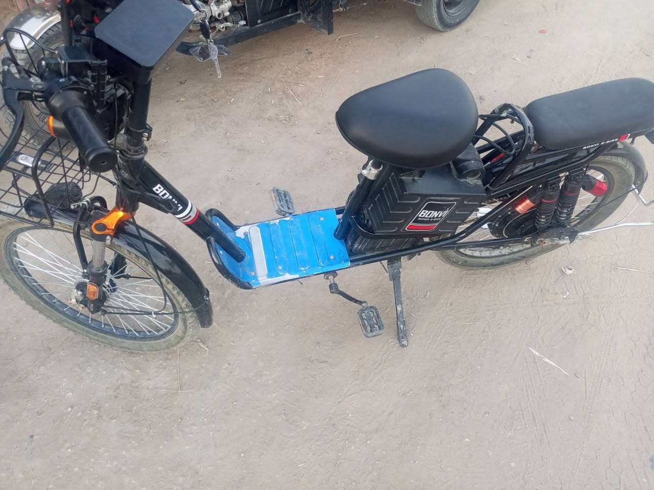 دراجة كهربائية (E-Bike) من فئة "الموبد/السكوتر الكهربائي المزود بدواسات".
تفاصيل الدراجة والموديل:
العلامة التجارية: BONVI (بونفي).
الطراز / الموديل: BONVI 80 (كما هو موضح على غطاء السلسلة وإطار البطارية).
أبرز المزايا والمواصفات الظاهرة:
نظام الدفع: هجين يجمع بين المحرك الكهربائي الخلفي (Rear Hub Motor) والدواسات العادية لاستخدامها عند نفاد البطارية أو للمساعدة.
البطارية: صندوق بطارية قابل للإزالة مثبت منتصف الدراجة أسفل المقعد الرئيسي.
نظام التعليق: مساعدات صدمات أمامية وخلفية مزدوجة (Dual Suspension) لامتصاص الصدمات أثناء القيادة.
التجهيزات والراحة:
مقعد إضافي للراكب الخلفي مزود بمسند ظهر.
سلة معدنية أمامية للتخزين.
دواسات إضافية لأقدام الراكب الخلفي.
شاشة/عداد سرعة ومفاتيح تحكم مع إشارات على المقبض الأمامي
للتواصل ***********
