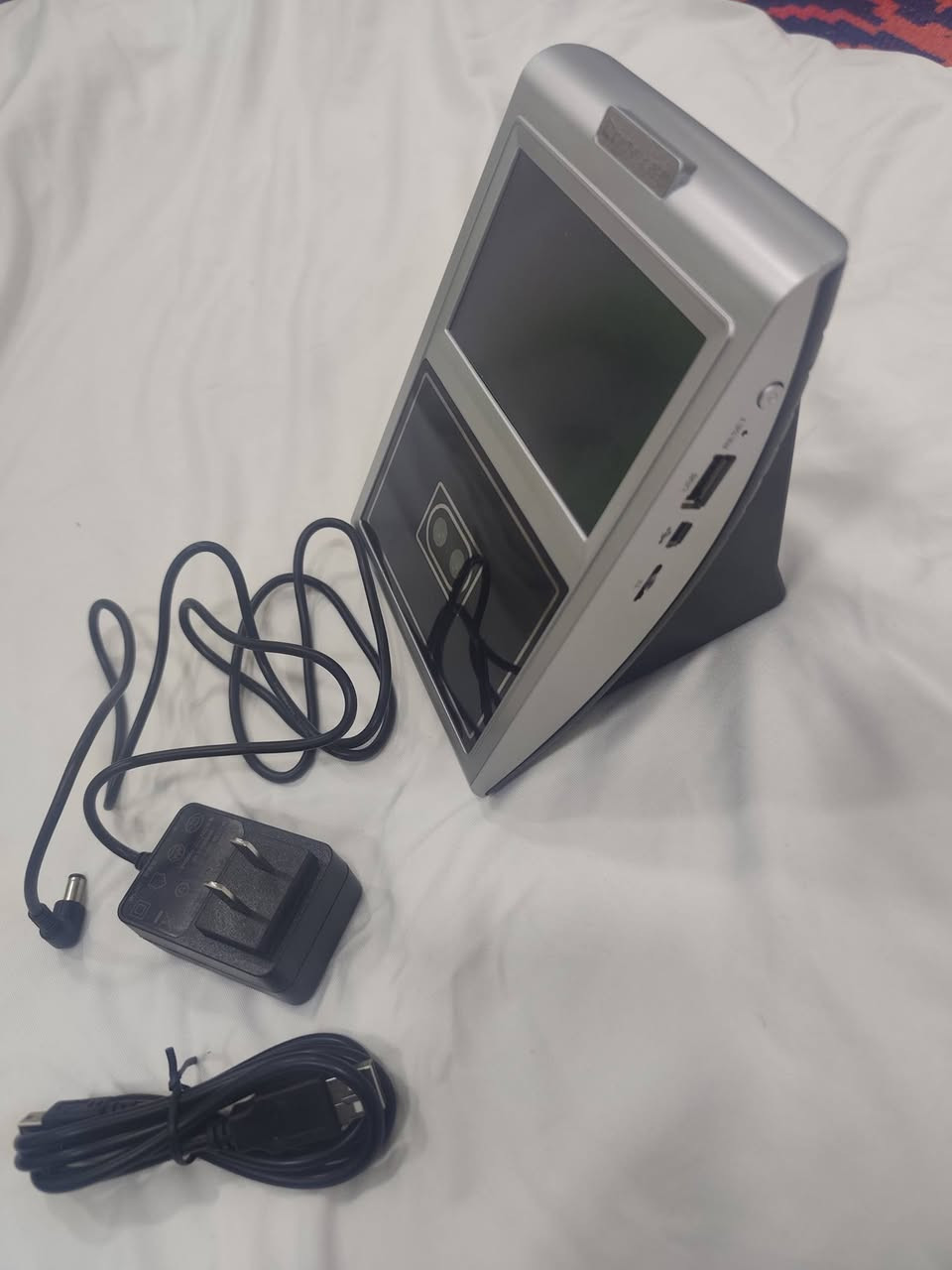 ا الجهاز هو جهاز بصمة الوجه (Face Recognition Terminal) من ماركة Comix، وهو مخصص لإدارة الحضور والانصراف للموظفين أو للتحكم في الدخول (Access Control).
إليك التفاصيل التقنية والوظائف بناءً على الصور المرفقة:
1. الوظائف الأساسية للجهاز
التعرف على الوجه: يستخدم الكاميرات المزدوجة والحساسات الضوئية (المصابيح الأرجوانية الظاهرة في الصور) للتعرف على ملامح الوجه بدقة، حتى في الإضاءة المنخفضة.
تسجيل الحضور والانصراف: يتيح للموظفين تسجيل وقت الدخول والخروج بمجرد الوقوف أمام الجهاز.
إدارة البيانات: يحتوي على قائمة "Report" لاستخراج تقارير الحضور مباشرة، وقائمة "Schedule" لضبط مواعيد العمل والنوبات.
2. المواصفات الظاهرة
الشاشة: شاشة ملونة تعمل باللمس لعرض القوائم والتعليمات.
المنافذ الجانبية:
USB: لسحب التقارير على "فلاش ميموري" أو تحديث النظام.
Mini USB: للاتصال المباشر بالكمبيوتر.
فتحة الطاقة: لتوصيل المحول الكهربائي (5 فولت غالباً).
زر Reset: لإعادة تشغيل الجهاز في حال حدوث تعليق.
3. شرح أيقونات القائمة الرئيسية
كما يظهر في الصورة الثالثة:
User: لإضافة موظف جديد، التقاط صورته، أو تعديل بياناته.
Schedule: لضبط ساعات العمل الرسمية والعطلات.
Report: لاستخراج جداول الحضور بصيغة Excel.
System: لضبط الوقت والتاريخ، اللغة، وإعدادات الشبكة.
Bell: لضبط تنبيهات صوتية (جرس) في أوقات معينة.
User Info: لعرض سجلات الموظفين المسجلين حالياً.


**إذا كنت صاحب هذا الإعلان وتريد حذفه لأي سبب، رجاءا أرسل رسالة إلى الدعم الفني**