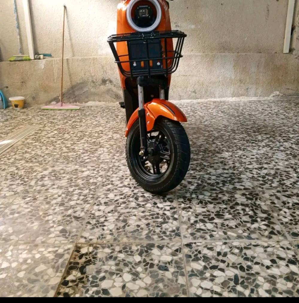 دراجة نارية كهربائية برتقالية بحالة ممتازة. تمتاز بسهولة القيادة وتوفير الوقود، مثالية للأستخدام اليومي في المدينة. الديكورات والإطارات في حالة جيدة، مع مقعد مريح وكبير يناسب جميع الأعمار.