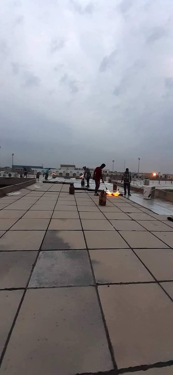 خليني أوضحلك: البيتومين المؤكسد وشنو علاقته بالايزوكام والعوازل وحماية الأسطح الخرسانية من  الرطوبه,,,,,,***********
1. مادة الإيزوكام (Isocam)
هي ألواح أو لفائف عزل بيتومينية (bituminous membrane) غالبًا مكونة من طبقتين أساسيتين:
1. البيتومين المؤكسد أو المعدل (Bitumen) → مادة عازلة ضد الماء.
2. طبقة تسليح من البوليستر أو الألياف الزجاجية (Fiberglass/Polyester) → تعطيها قوة شد ومتانة.
يتم توريدها عادة على شكل رولات يتم تسخينها بالغاز (تورش Torch) ثم لصقها على الأسطح.
أهم استخداماتها:
أ / عزل الأسطح الخرسانية.
ب / عزل الأساسات والجدران الملامسة للتربة.
ج /  عزل الحمامات والخزانات.
.مميزاتها:
أ (مقاومة ممتازة لتسرب المياه.)

ب (عمر افتراضي طويل (10–20 سنة حسب الجودة).

ج (تتحمل الظروف المناخية والحرارة.

2. عوازل اللباد (Felt Insulation / Roofing Felt)

اللباد يُستخدم عادة كطبقة عازلة أو حاجز إضافي.
يتكون من ألياف عضوية أو صناعية مشبعة بالبيتومين.
يأتي أيضًا بشكل لفائف، ولكنه أخف وأقل سماكة من الإيزوكام.
يستخدم في:
كطبقة تحتية قبل وضع القرميد أو الأسقف المعدنية.
أحيانًا كطبقة إضافية فوق أو تحت ألواح العزل البيتوميني.
مميزاته:
أ / سهل التركيب ورخيص نسبيًا.
ب / يعمل كحاجز أولي للرطوبة.
عيوبه:
1 أقل متانة وعمره الافتراضي أقصر من الإيزوكام.
2 قد يتأثر بسرعة بأشعة الشمس والحرارة إذا لم يُغطى بطبقة حماية.
📌 الخلاصة: 
1 الإيزوكام = عازل بيتوميني قوي ضد الماء والرطوبة (حل نهائي للأسطح والخزانات).
2 اللباد = طبقة مساعدة أو ثانوية، جيدة ولكنها ليست بديلة عن الإيزوكام في العزل طويل الأمد. يوجد واتساب 

*********** حلة, بابل
