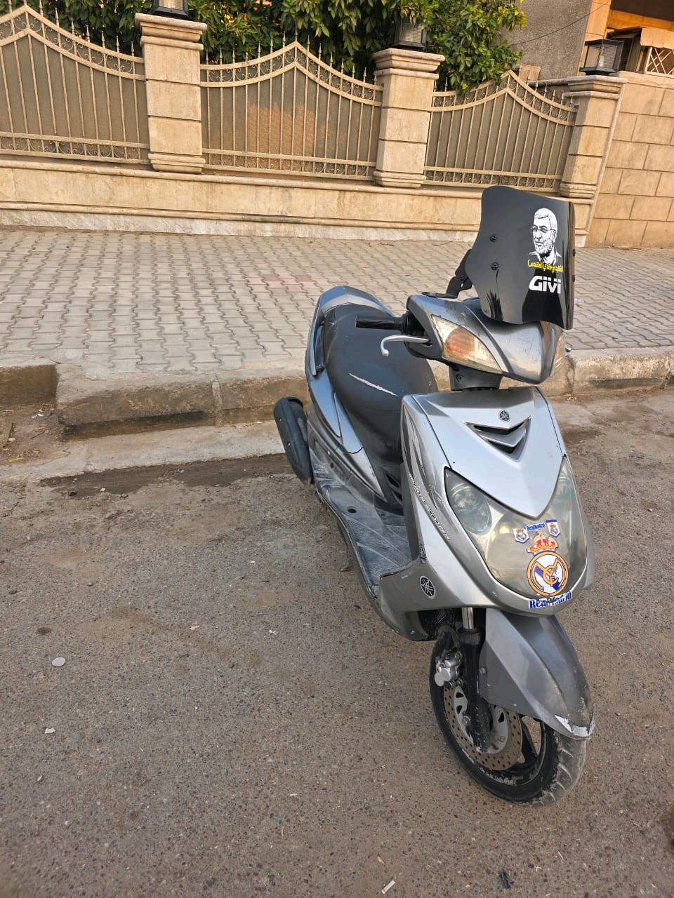 دراجة نارية نوع ياماها بحالة جيدة، مع ملصقات تضيف لها لمسة رياضية. الدراجة مزودة بزجاج واقٍ للرياح. عداد الكيلومترات يبين الاستخدام الجيد حيث تظهر القراءة مدى المحافظة عليها. مناسبة للتنقل اليومي في المدينة بسرعة وأمان.