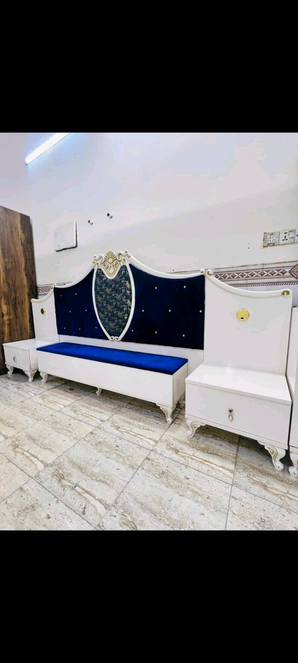 غرفة نوم فاخرة بتصميم كلاسيكي تشمل سرير مريح مع لوح أمامي مبطن باللون الأزرق الداكن وخزانة ملابس كبيرة مع مرايا زخرفية. تتميز الغرفة بتفاصيل ذهبية على الأبواب والأدراج، مما يضفي لمسة من الفخامة والرقي. الطقم يشمل أيضًا تسريحة مع مرآة كبيرة وكرسي مبطن لتوفير الراحة أثناء التحضير اليومي. الأثاث مصنوع بجودة عالية ويضفي لمسة فنية على أي غرفة نوم.