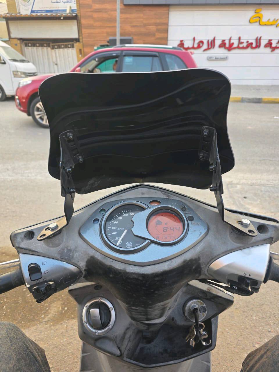 دراجة نارية نوع ياماها بحالة جيدة، مع ملصقات تضيف لها لمسة رياضية. الدراجة مزودة بزجاج واقٍ للرياح. عداد الكيلومترات يبين الاستخدام الجيد حيث تظهر القراءة مدى المحافظة عليها. مناسبة للتنقل اليومي في المدينة بسرعة وأمان.