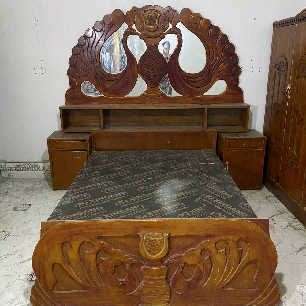 غرفة نوم خشبية كلاسيكية مكونة من سرير مع مرآة فاخرة ودولاب مكون من عدة أبواب. التصميم يحتوي على حفرات ونقوش جميلة تضيف لمسة مميزة للغرفة. الأثاث بحالة جيدة ومناسب لإضافة جمالية لأي غرفة نوم.