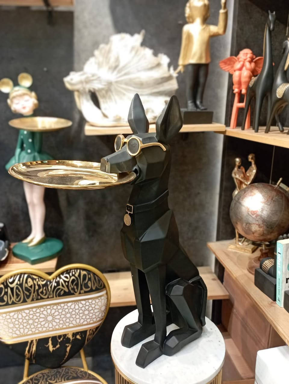 هذا المجسم هو تمثال ديكور لكلب من فصيلة "دوبيرمان" مصمم بأسلوب هندسي عصري (Origami/Geometric) ويُستخدم كطاولة جانبية أو حامل للأغراض. 
 +1
إليك أبرز تفاصيل هذا المنتج:
الوظيفة: يعمل كستاند للمفاتيح، المجوهرات، أو كطاولة خدمة صغيرة للوجبات الخفيفة والمشروبات بفضل الصينية المعدنية.
المادة: يُصنع غالباً من مادة الراتنج (Resin) المتينة عالية الجودة، مع صينية قابلة للفصل.
التصميم: يتميز الكلب بمظهر "جنتلمان" حيث يرتدي نظارات وربطة عنق، مما يضفي لمسة عصرية وأنيقة السعر 90 ألف


**إذا كنت صاحب هذا الإعلان وتريد حذفه لأي سبب، رجاءا أرسل رسالة إلى الدعم الفني**