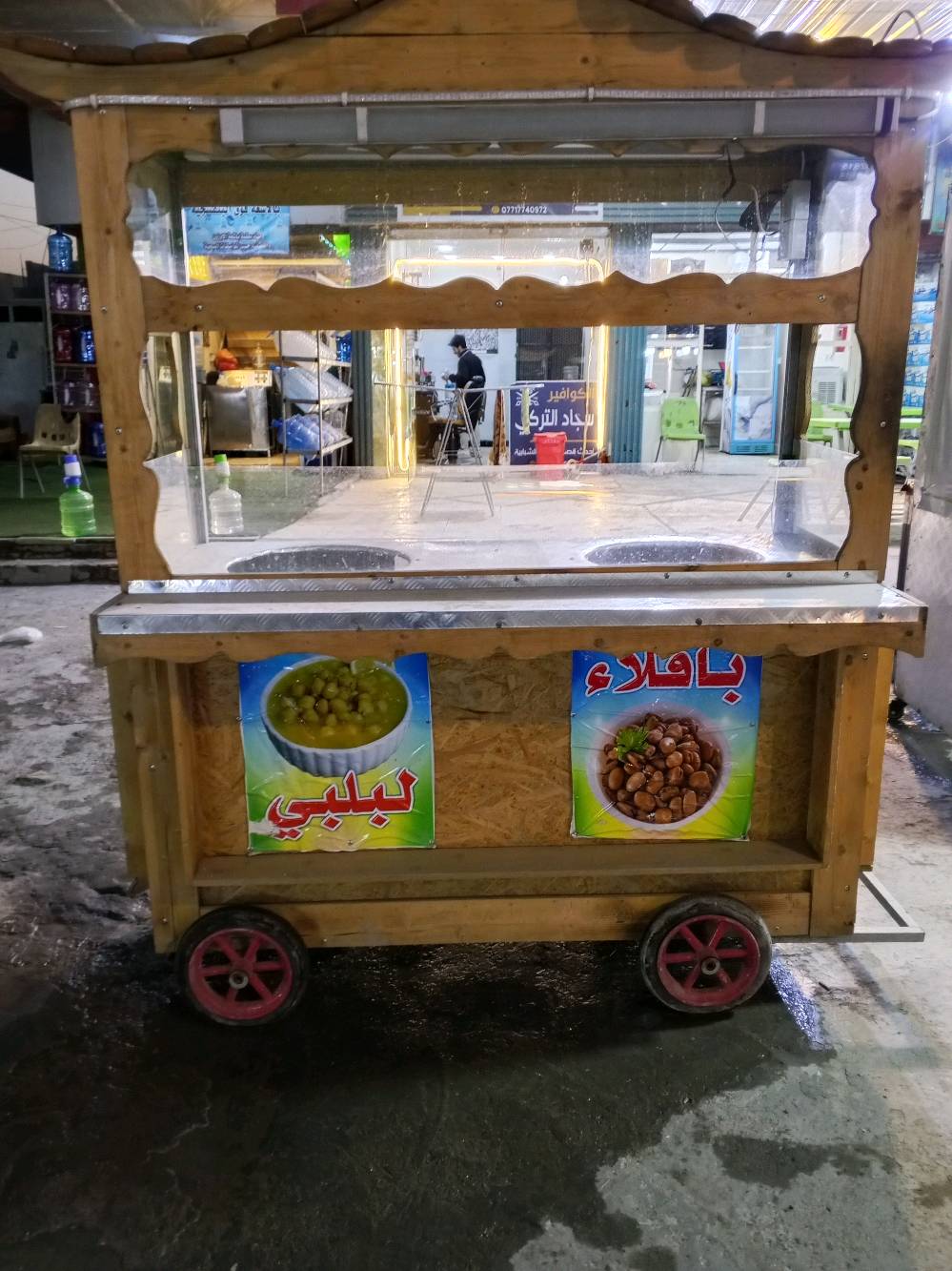 عربانة للبيع مخصصة لبيع الباقلاء والبلبي. تصميم قوي ومتين مع عجلات حديدية سهلة النقل. تحتوي على قسمين لتسخين الطعام وحماية من الزجاج.