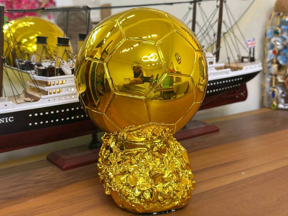 مجسم الكرة الذهبية (Ballon d'Or) الفاخر 
​عش شغف كرة القدم واقتنِ رمز التفوق الأسطوري! نقدم لكم مجسم "الكرة الذهبية" بتصميمه المذهل وتفاصيله الدقيقة، ليكون القطعة الأبرز في غرفتك، مكتبك، أو الهدية المثالية لعشاق الساحرة المستديرة. هذا المجسم ليس مجرد زينة، بل هو تحفة فنية تعكس روح الانتصار والبطولة.
​ أبرز مميزات المجسم:
​وزن ثقيل واحترافي: يتميز المجسم بـ وزن ثقيل يمنحه طابعاً احترافياً وقيمة عالية عند حمله، مما يجعله يحاكي شعور حمل الجوائز الحقيقية الفاخرة.
​طلاء ذهبي شديد اللمعان: يتمتع بلمسة ذهبية براقة وعاكسة للضوء بجودة استثنائية (كما يظهر بوضوح في الصور)، مما يضفي عليه مظهراً خاطفاً للأنظار.
​دقة في التفاصيل: تصميم الكرة يحمل تقطيعات سداسية مطابقة للواقع، مع نقش بارز وواضح لشعار "BALLON D'OR" على الواجهة.
​قاعدة فنية متينة: يستند المجسم على قاعدة صلبة ذات ملمس صخري ذهبي فريد، تزيد من ثباته وتضيف لمسة جمالية مضاعفة.
​لوحة إهداء مخصصة: تحتوي القاعدة على مساحة مستطيلة ناعمة وفارغة، وهي مثالية لحفر اسمك، اسم فريقك، أو كتابة إهداء خاص لشخص عزيز.
​الاستخدامات المثالية:
​هدية استثنائية: الخيار الأول والأفخم لأي شخص مهووس بكرة القدم (سواء كان لاعباً أو مشجعاً).
​ديكور فخم: يضيف طابعاً رياضياً أنيقاً عند وضعه على أرفف العرض، المكاتب، أو بجانب مقتنياتك الثمينة.
​جوائز البطولات: قطعة التتويج المثالية للبطولات المحلية، الدوريات الرمضانية، أو مسابقات البلايستيشن بين الأصدقاء.
السعر المذهل:
​احصل على هذه التحفة الفنية بسعر تنافسي جداً:
18,000 فقط!
​اطلبها الآن وتوج نفسك أو من تحب بأعرق جوائز كرة القدم!