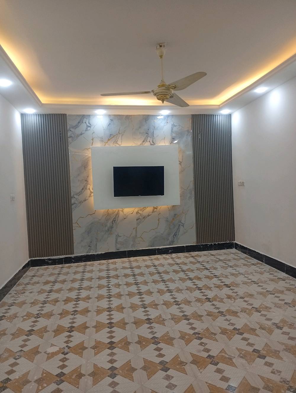 غرفة استقبال حديثة للبيع، تتميز بتصميم عصري أنيق مع إضاءة مخفية وجدارية رخامية تعطي لمسة فاخرة للديكور. الأرضية مزينة ببورسلين عالي الجودة بلون جذاب. الغرفة تحتوي على مروحة سقف لضمان التهوية الجيدة.