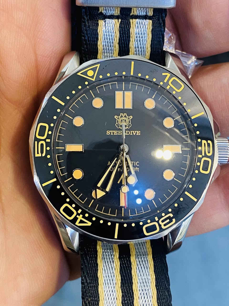 هذه الساعة هي Steeldive SD1957، وهي ساعة غوص أوتوماتيكية تُعتبر "Homage" (ساعة مستوحاة في تصميمها) لساعة أوميغا الشهيرة "No Time To Die"

أبرز مواصفات هذه الساعة:
* الحركة: تعمل بحركة أوتوماتيكية من نوع Seiko NH35 التي تدعم خاصية التعبئة اليدوية وإيقاف الثواني (Hacking).��
* مقاومة الماء: تصل قدرتها على مقاومة الماء إلى 300 متر. ��
* الزجاج: تأتي بزجاج من كريستال الياقوت (Sapphire Crystal) المطلي بطبقة مضادة للانعكاس. ��
* الهيكل والقياس: يبلغ قطر الهيكل 42 ملم، وهو مصنوع من الفولاذ المقاوم للصدأ. ��
* الإضاءة: تتميز بمادة Swiss C3 Super-LumiNovaالمضيئة على العقارب ومؤشرات الميناء لرؤية واضحة في الظلام.


**إذا كنت صاحب هذا الإعلان وتريد حذفه لأي سبب، رجاءا أرسل رسالة إلى الدعم الفني**