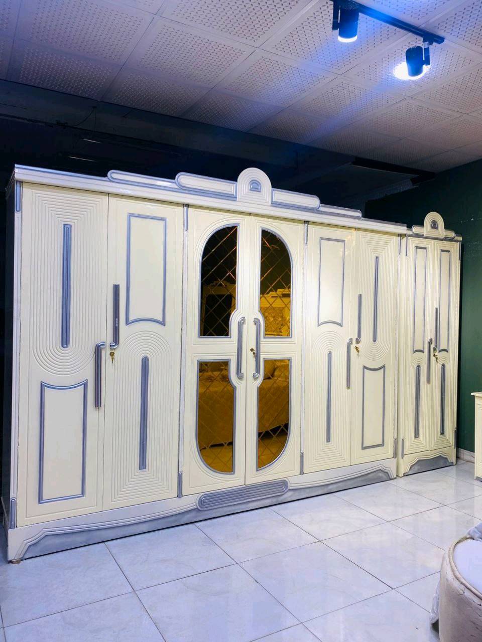 غرفة نوم فاخرة بتصميم كلاسيكي جذاب تتميز بمظهر أنيق وفخم. تضم سرير واسع ودولاب ملابس كبير مع مرايا، بالإضافة إلى طاولة زينة ودواليب جانبية بنفس التصميم. الخامات المستخدمة تعطي مظهر دافئ ومريح، مثالي لإضفاء لمسة من الفخامة في غرفة نومك.