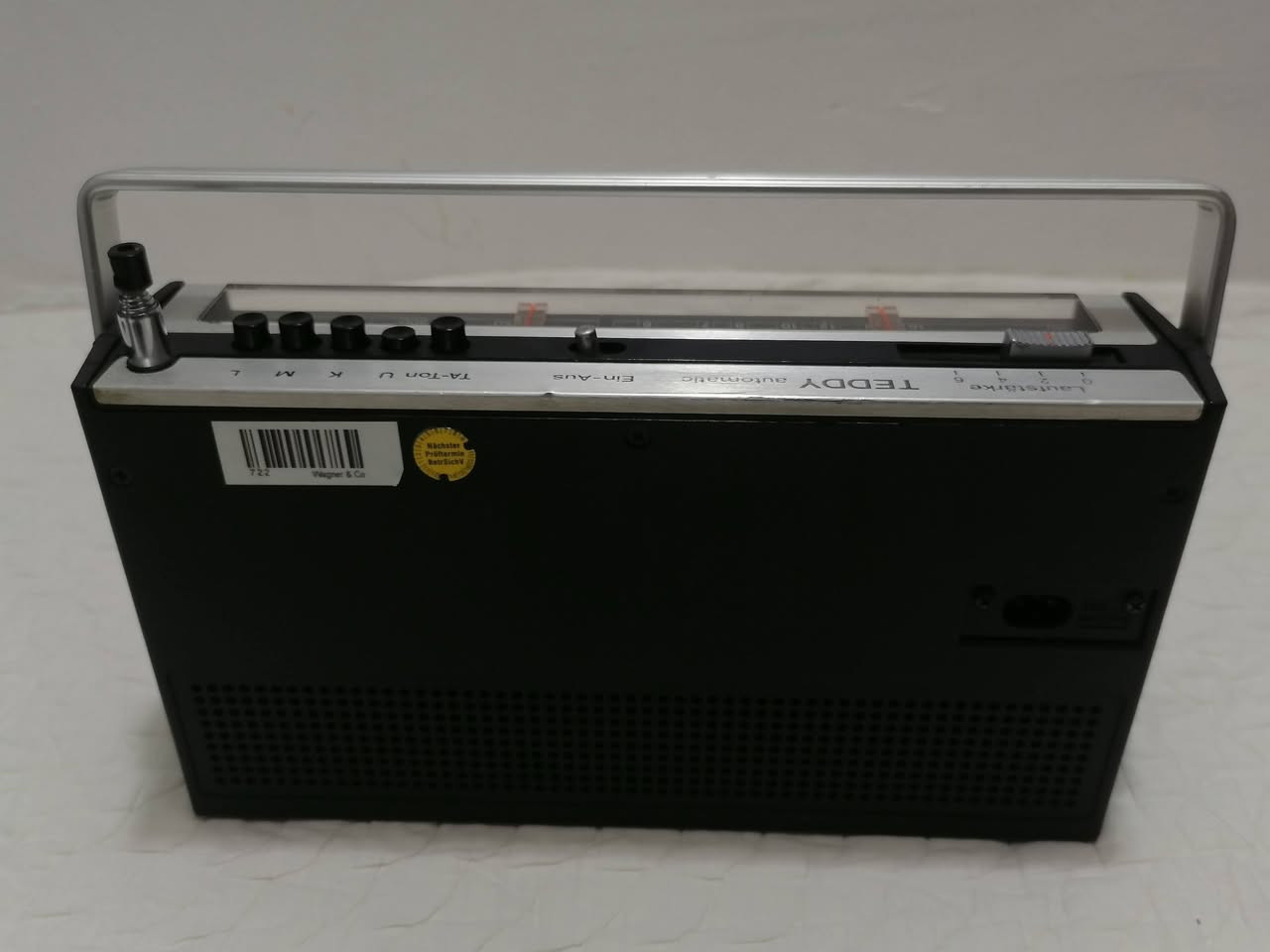 هذا الجهاز هو راديو ترانزستور كلاسيكي من نوع ITT Schaub-Lorenz Teddy automatic 103، وهو إصدار ألماني الصنع يعود لفترة أوائل السبعينيات (تحديداً بين عامي 1972 و1974).
يُعرف هذا الموديل بتصميمه العتيق (Vintage) الذي يجمع بين البلاستيك واللمسات الخشبية على الواجهة الأمامية. 
المواصفات التقنية الرئيسية:
نطاقات الموجات: يدعم استقبال موجات FM (أو UKW)، والموجات المتوسطة (MW)، والطويلة (LW)، والقصيرة (SW).
الطاقة: يعمل بالكهرباء المباشرة (110-240 فولت) أو عن طريق البطاريات (4 بطاريات وسط بقوة 1.5 فولت من نوع AA).
المكونات الداخلية: يحتوي على 11 ترانزستور، ويتميز بوجود هوائي تلسكوبي بطول 80 سم لاستقبال أفضل للموجات.
المنافذ: مزود بمقبس لسماعة الرأس (3.5 ملم) ومنفذ DIN خماسي لتوصيل مسجل صوت أو مشغل أقراص.
الأبعاد والوزن: يبلغ وزنه حوالي 1.2 كجم، وبأبعاد تقريبية 215 × 127 × 70 ملم. 
يُعتبر هذا الراديو قطعة "أنتيك" مميزة لهواة جمع الأجهزة القديمة، وغالباً ما يتم تداوله في أسواق التحفيات المستعملة .
العنوان بغداد - البياع موجود ***********‪ واتساب
