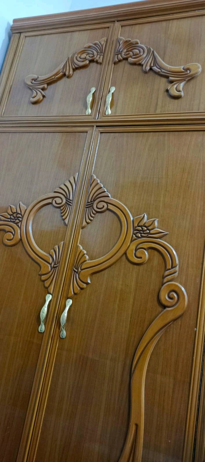 غرفة نوم خشبية أنيقة تتضمن دولاب كبير بتصميم مزخرف وسرير مزدوج مع كومودينة. الخشب مصقول وذو جودة عالية، والزخارف تضيف لمسة كلاسيكية للمكان. يناسب الغرفة الرئيسية ويضيف لمسة من الفخامة والراحة.